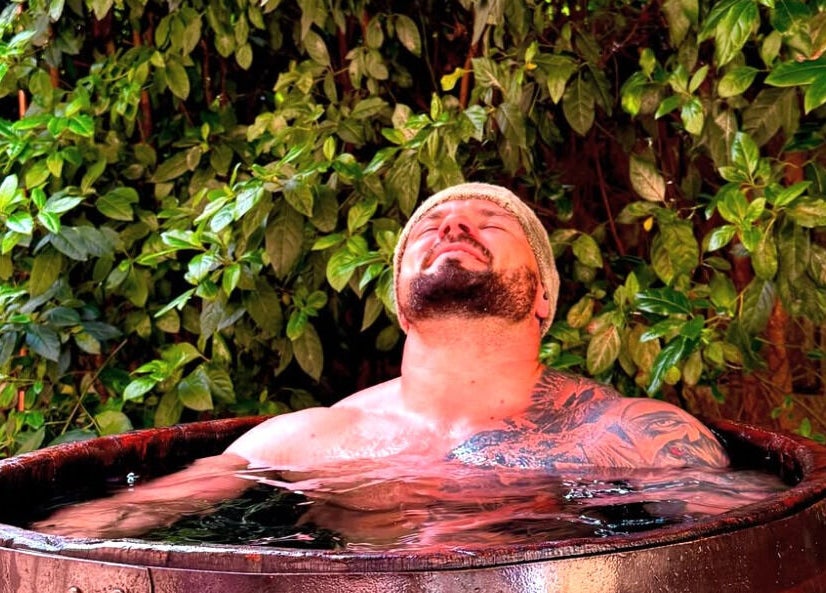 Man relaxes in a wooden tub amidst lush greenery at Phoenix Burning Sauna, London, England, GB.