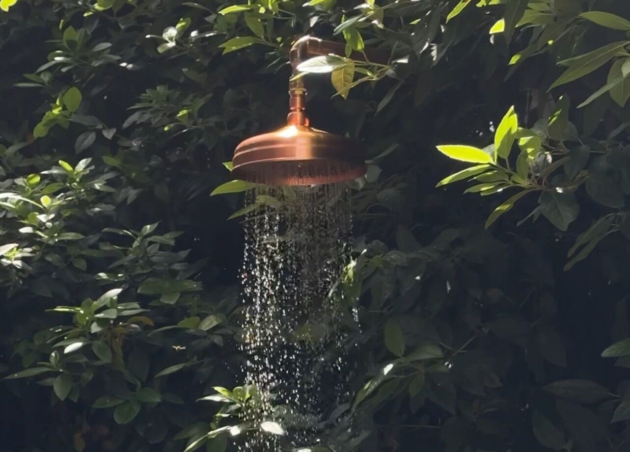 Outdoor copper shower at Phoenix Burning Sauna in London, England, GB, surrounded by lush green foliage.