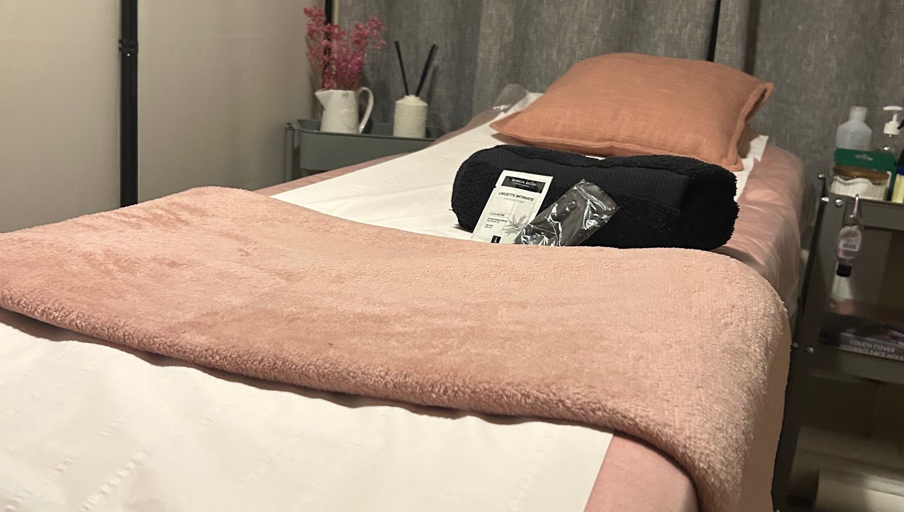 A peaceful waxing room at Bare & Bonnie Waxing in Banbury, England, GB with a neatly arranged bed and soft pink linens.