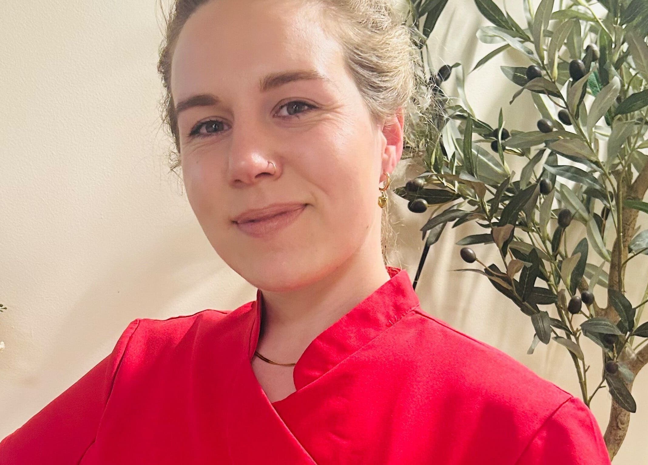 Staff member at Bare & Bonnie Waxing, Banbury, England, GB, in welcoming red attire and floral backdrop.
