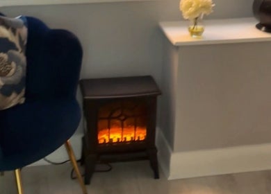 Elegant seating with floral cushion and electric fireplace at Bodmerised, Romford, England, GB.
