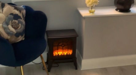 Elegant seating with floral cushion and electric fireplace at Bodmerised, Romford, England, GB.