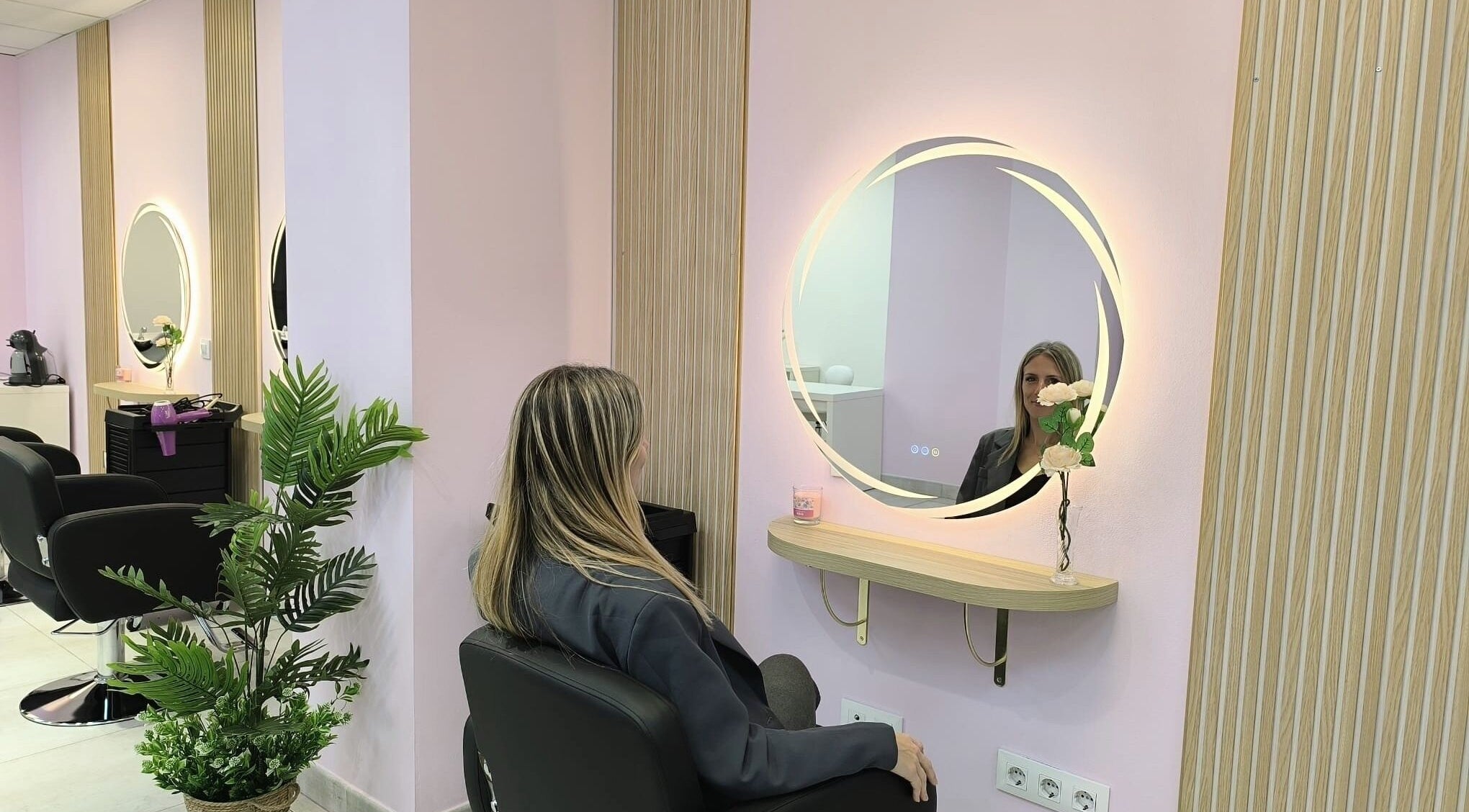 Interior de DS INNOVA STUDIO HAIR & NAILS en València, is ES, mujer frente a espejo circular iluminado.