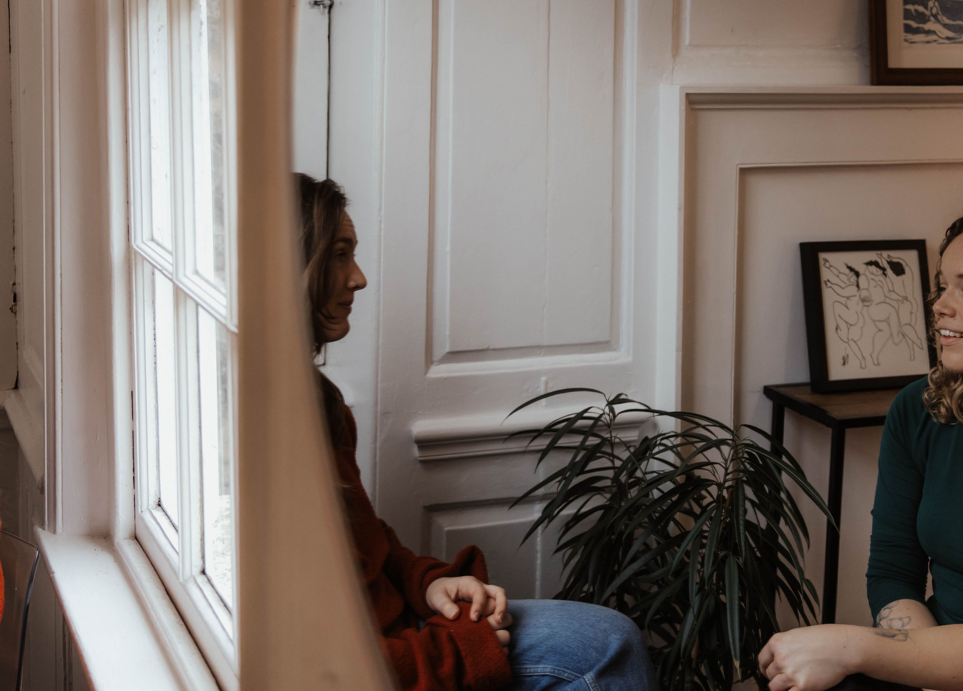 Two women chatting in a cozy room at The Elsewhere, Norwich, England, GB, with warm decor and art.