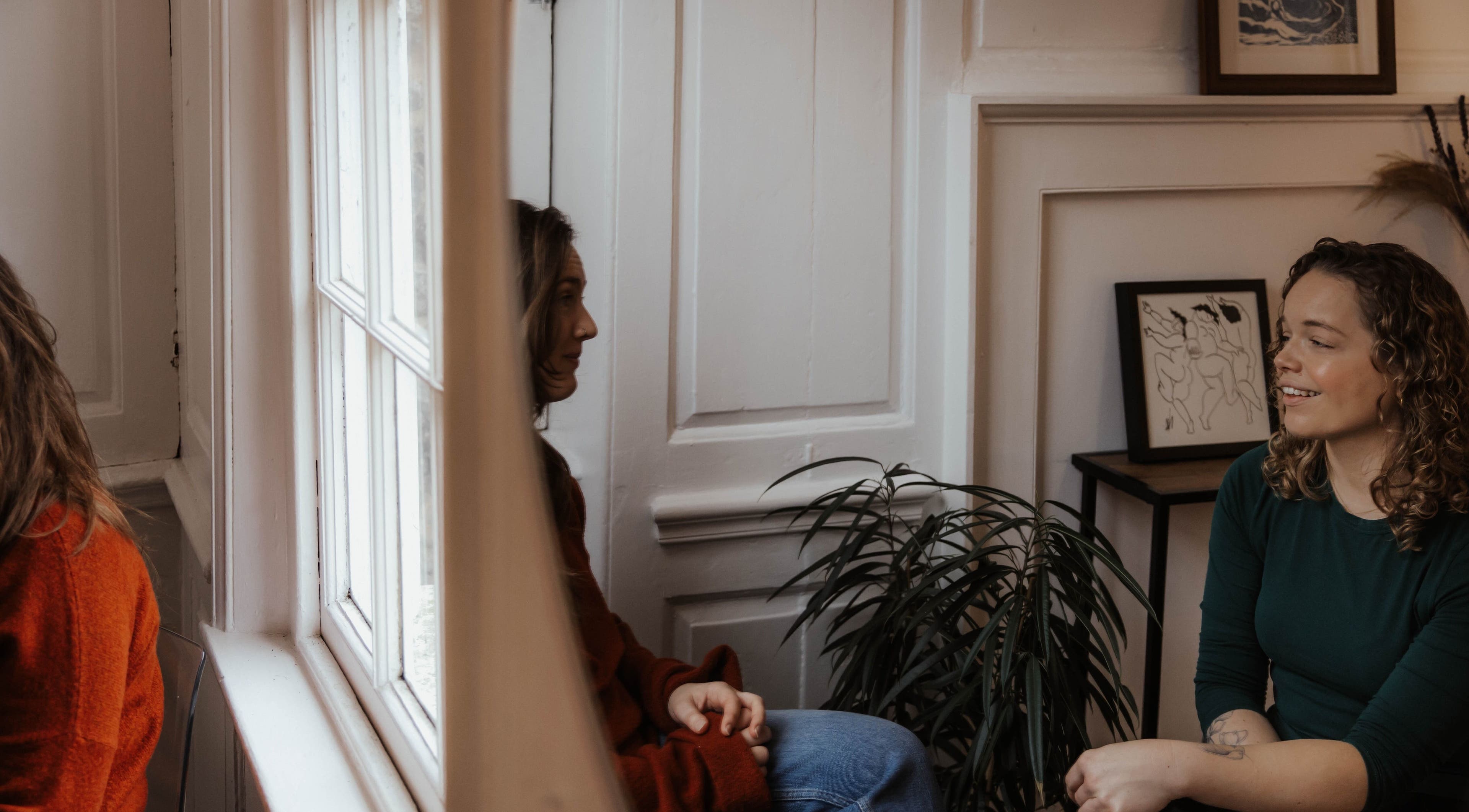 Two women chatting in a cozy room at The Elsewhere, Norwich, England, GB, with warm decor and art.