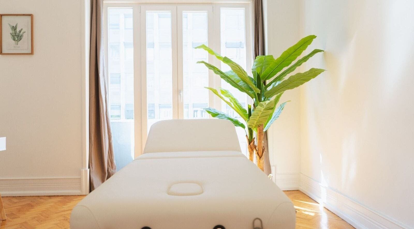 Sala de massagem iluminada no Wellzen by Diana, Lisboa, Lisboa, PT, com cama branca e planta decorativa.