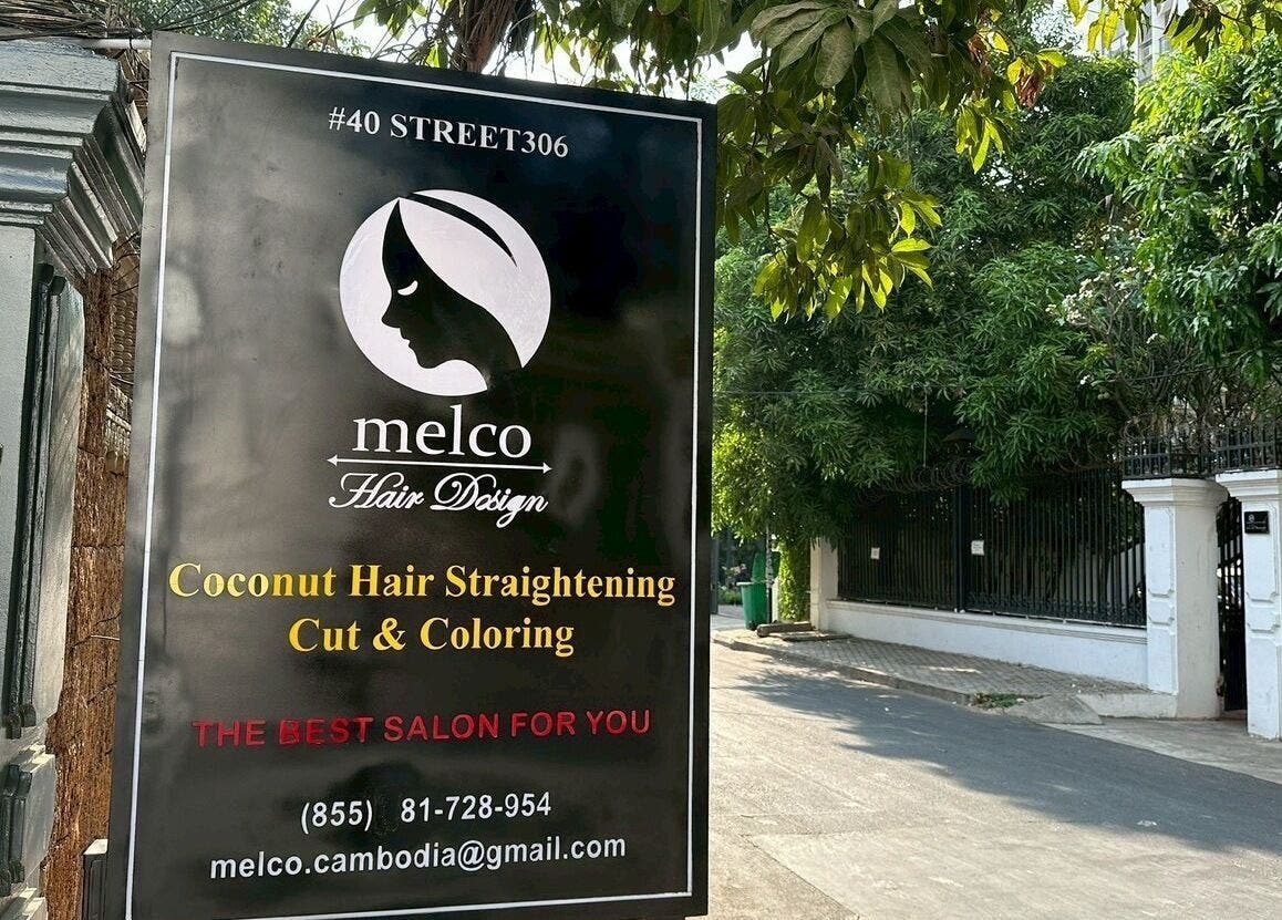 Outdoor sign for melco HairDesign, Phnom Penh, featuring hair services and contact details.