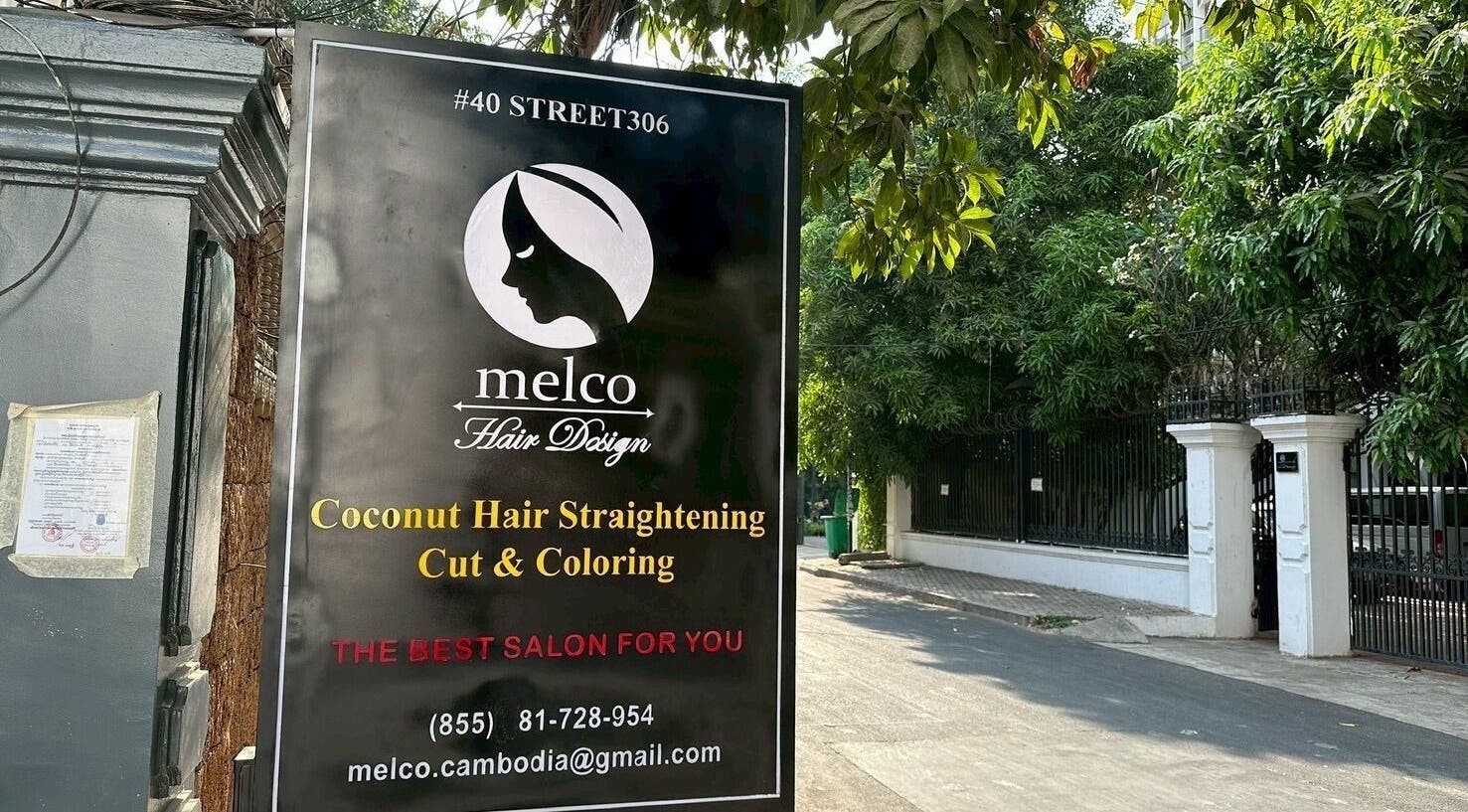 Outdoor sign for melco HairDesign, Phnom Penh, featuring hair services and contact details.