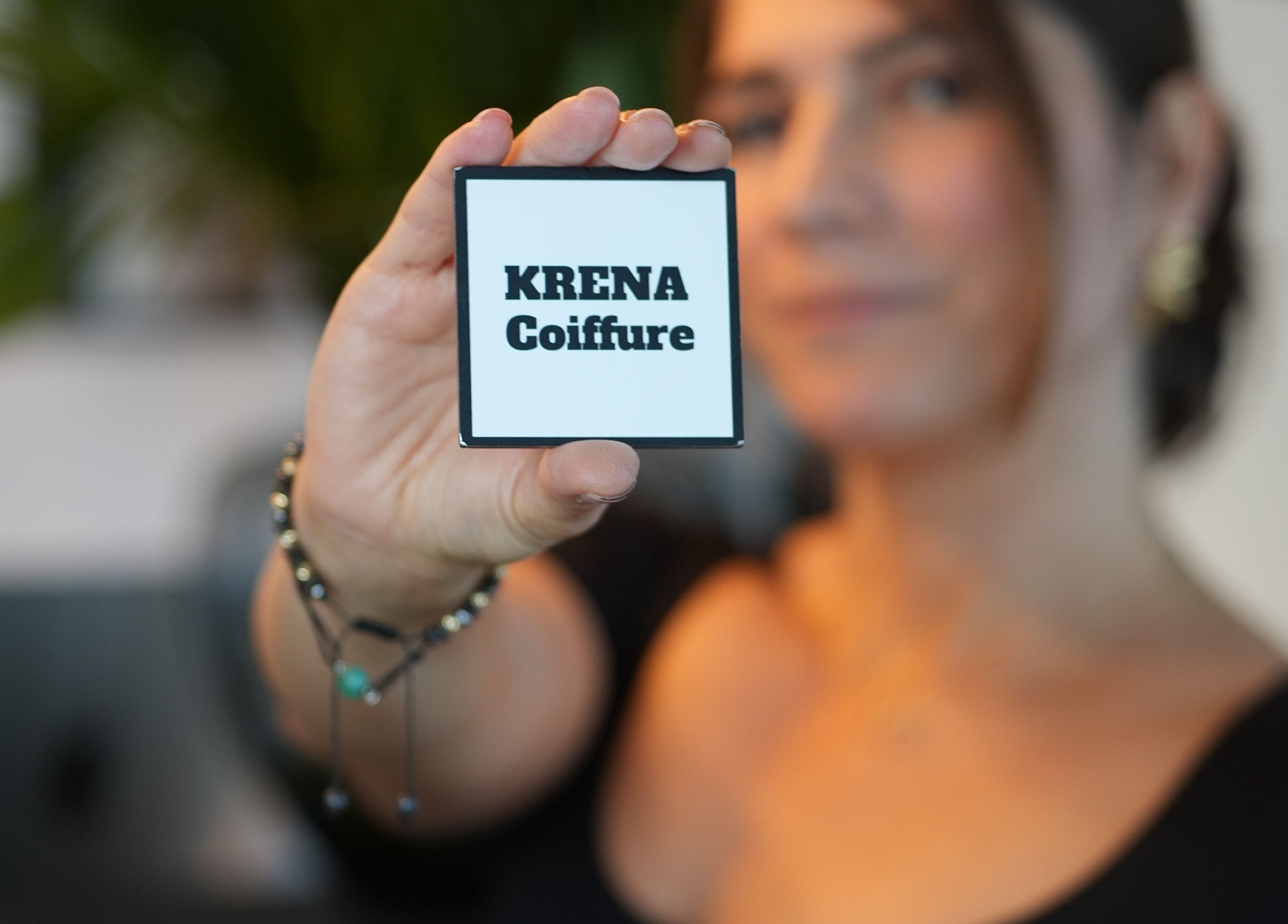 Carte KRENA Coiffure Maison Krena, Bruxelles, Bruxelles, BE, tenue par une main devant un visage flou.
