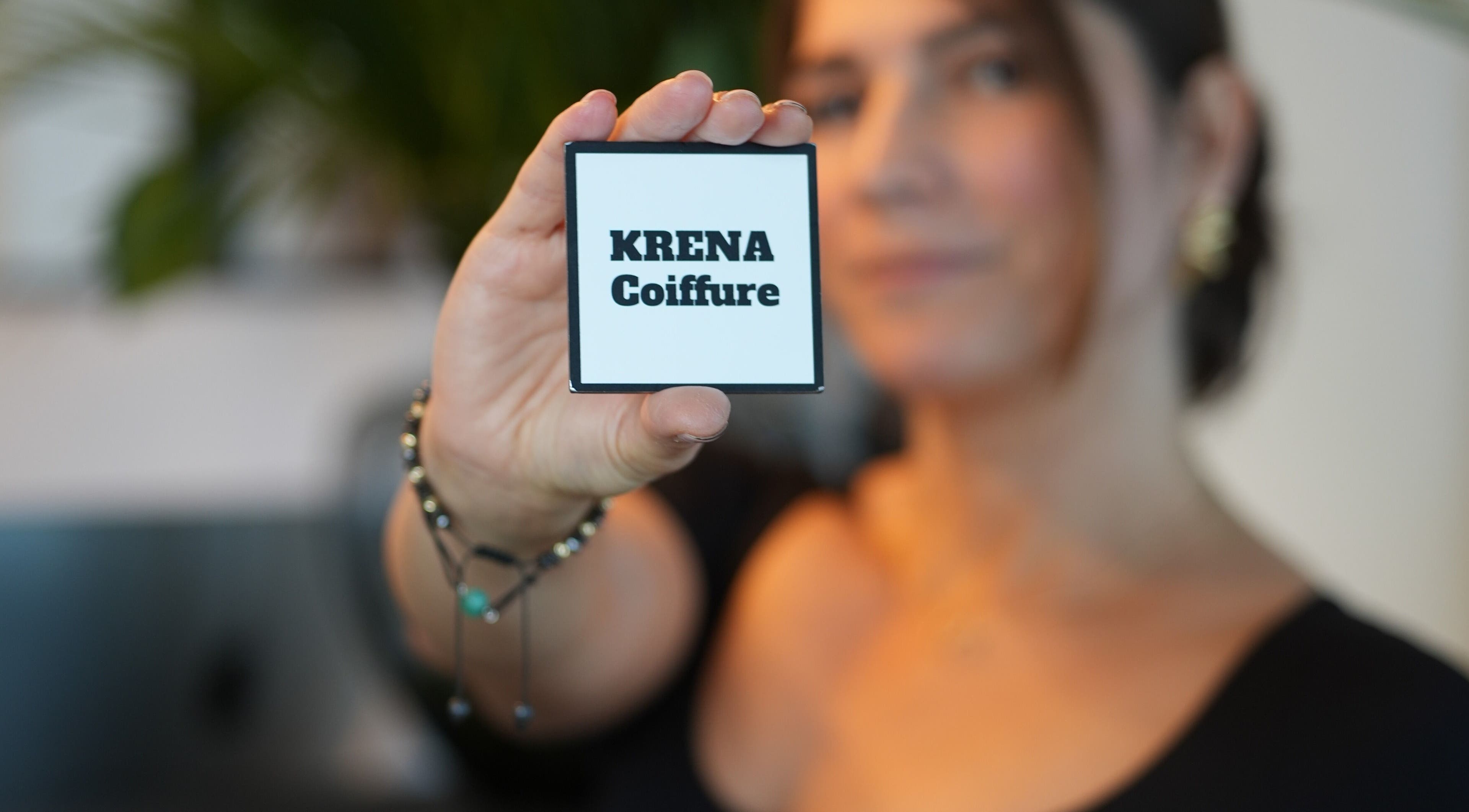 Carte KRENA Coiffure Maison Krena, Bruxelles, Bruxelles, BE, tenue par une main devant un visage flou.