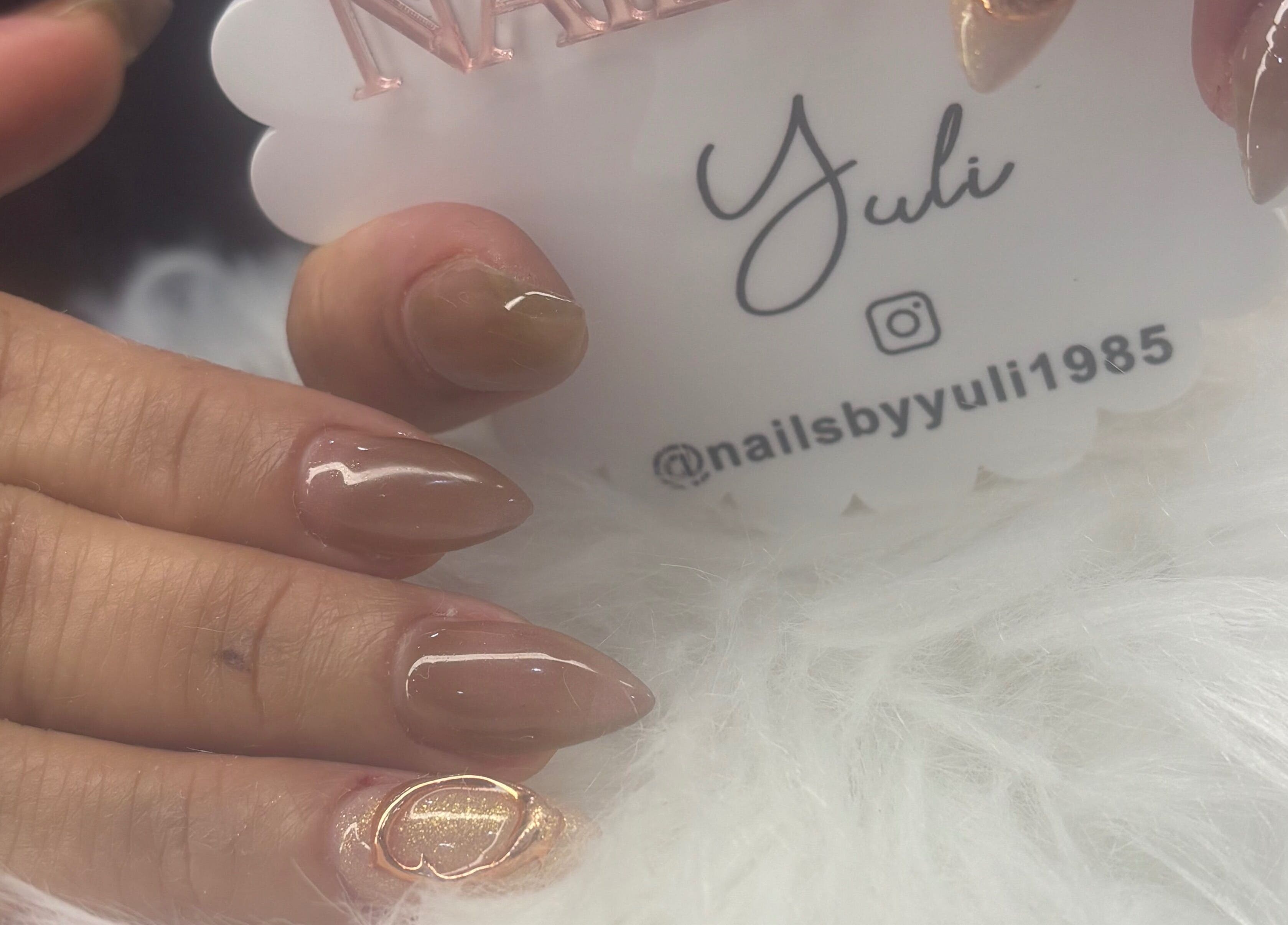 Close-up of elegant nude manicure at Nails by Yuli, Greenacres, Florida, US, with glossy finish and gold accent.