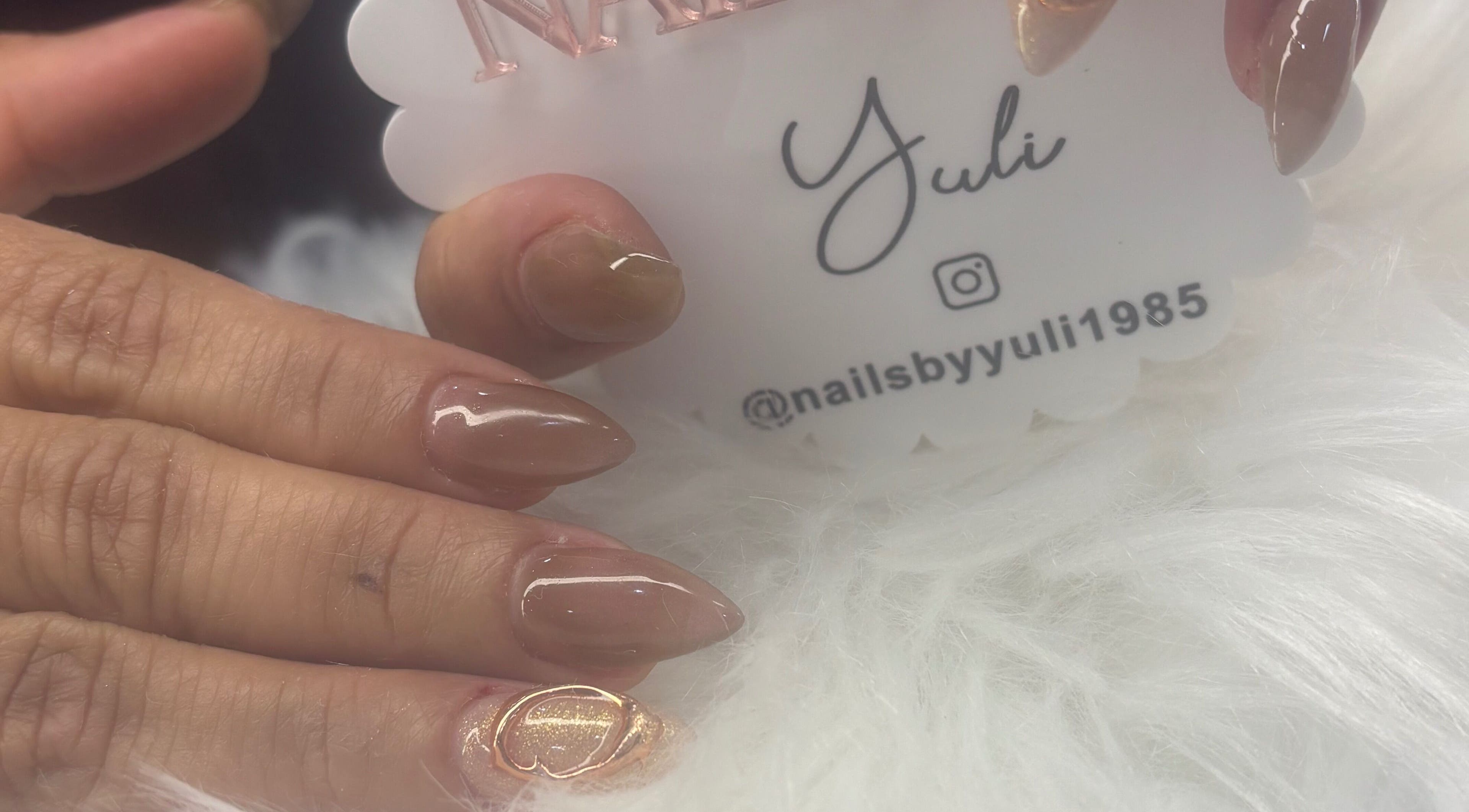 Close-up of elegant nude manicure at Nails by Yuli, Greenacres, Florida, US, with glossy finish and gold accent.