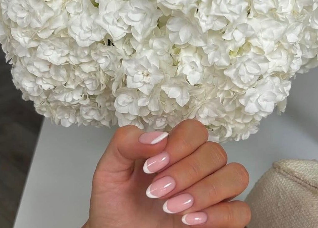 Elegant French manicure at Biab By Amber, Watford, GB with soft flowers in the background.