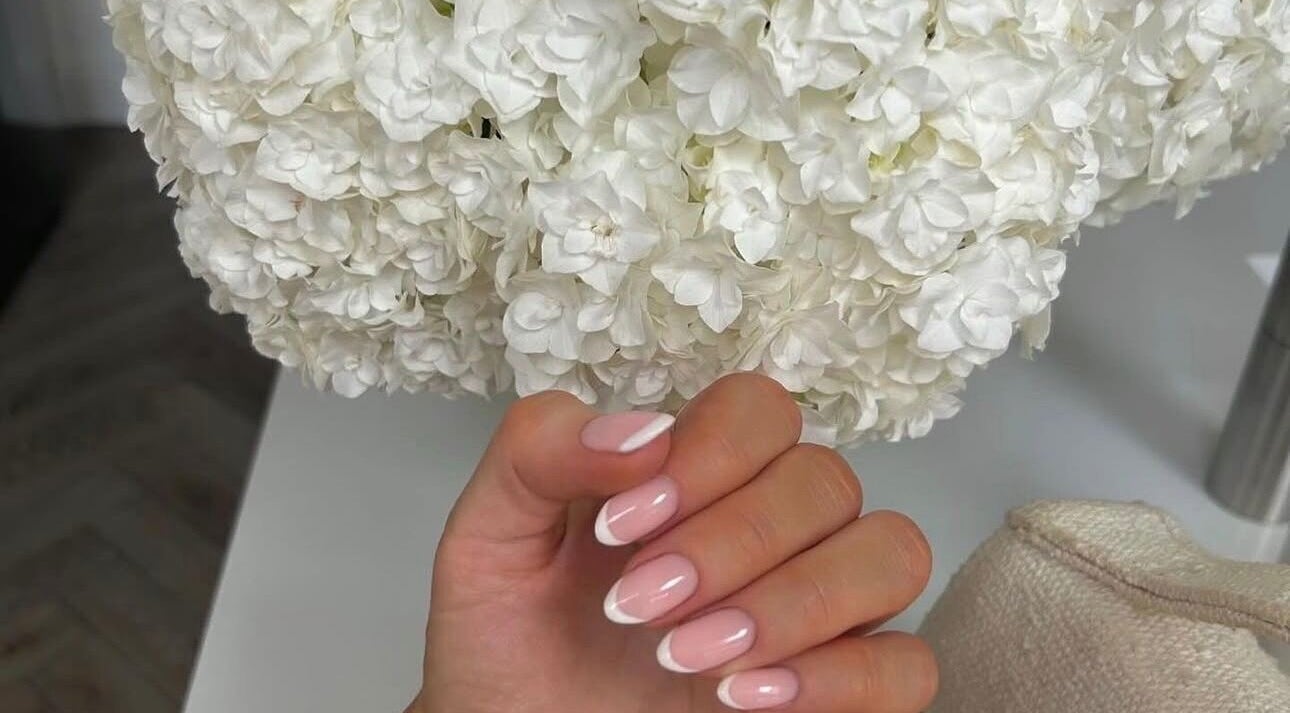 Elegant French manicure at Biab By Amber, Watford, GB with soft flowers in the background.