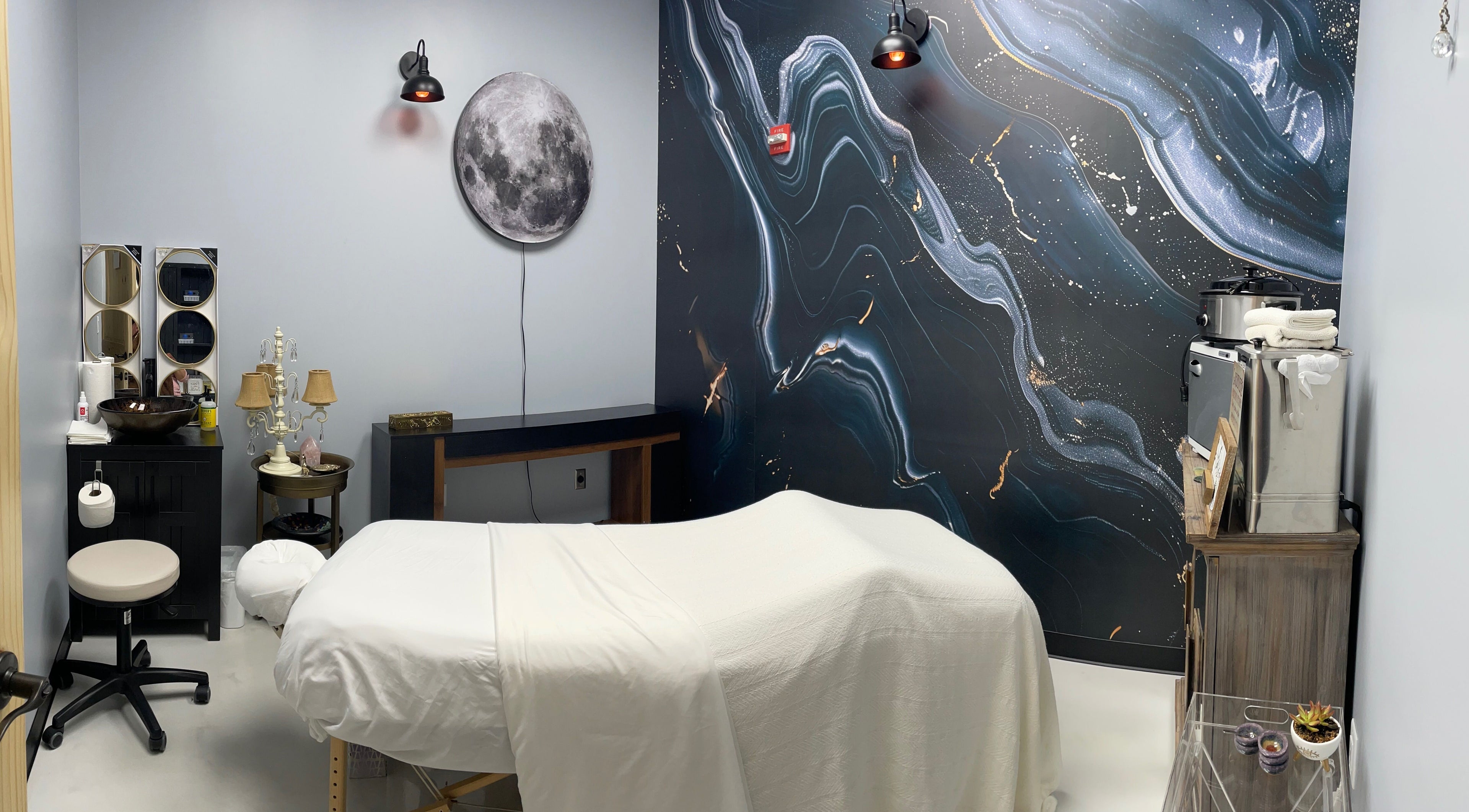 Tranquil spa room at AUM Body Bliss LLC, Saint Albans City, Vermont, with lunar wall art and a massage table.