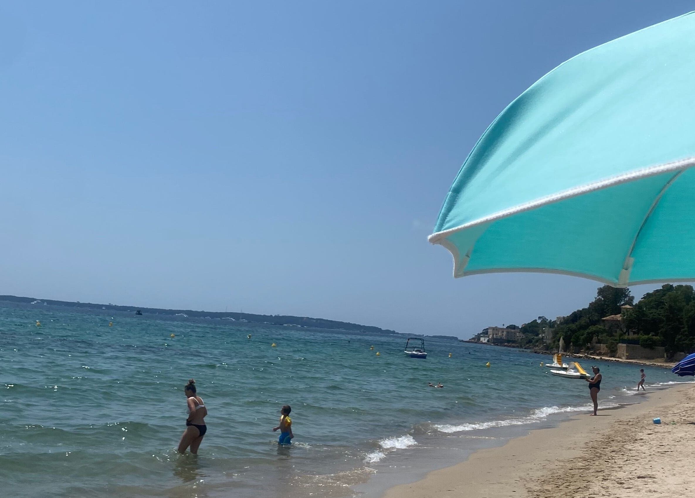 Beach scene near Tanlines IE with turquoise umbrella and visitors enjoying the waves.