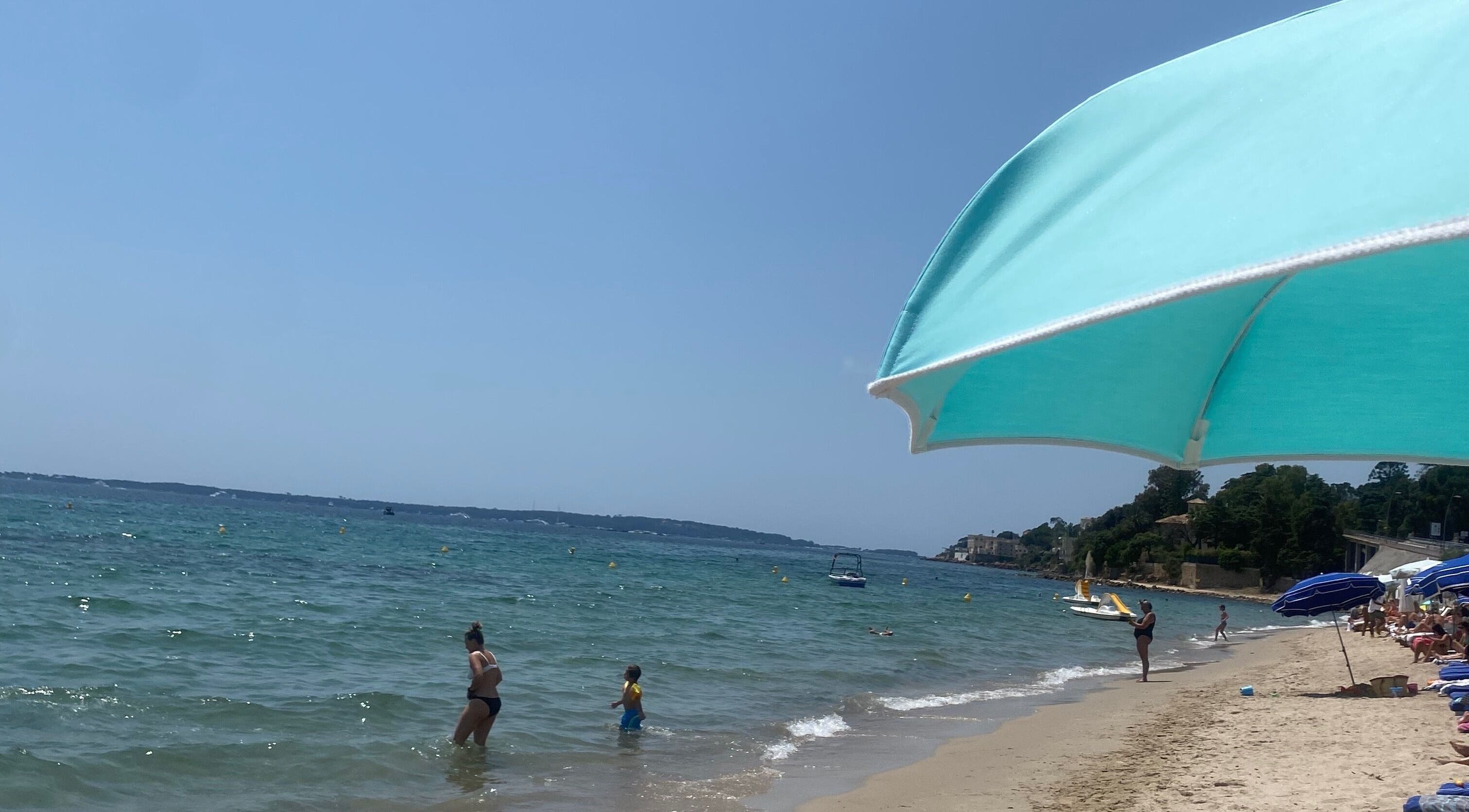 Beach scene near Tanlines IE with turquoise umbrella and visitors enjoying the waves.