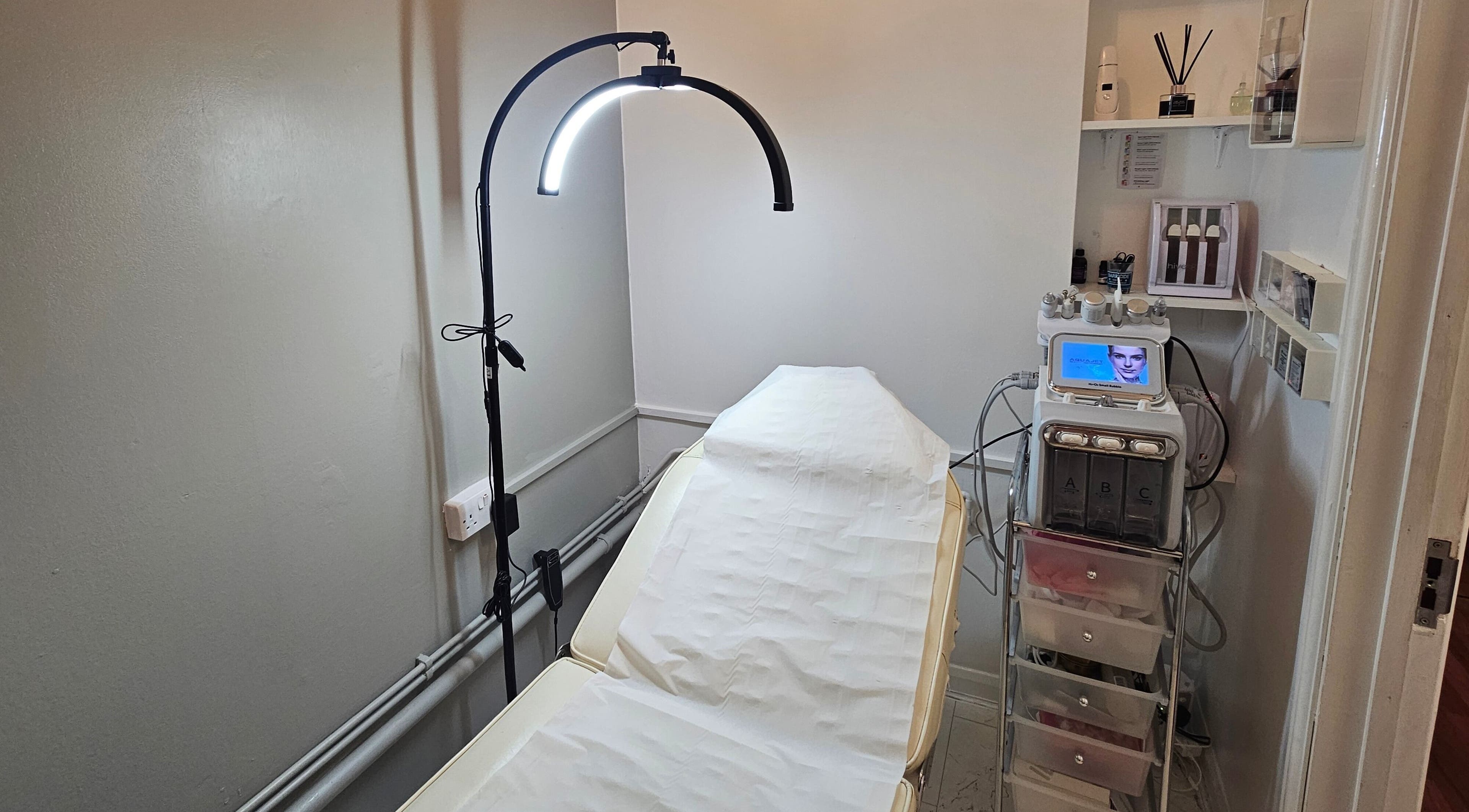 Treatment room at Pure Beauty Lounge in Hampton, England, GB, featuring a modern facial machine and therapy bed.