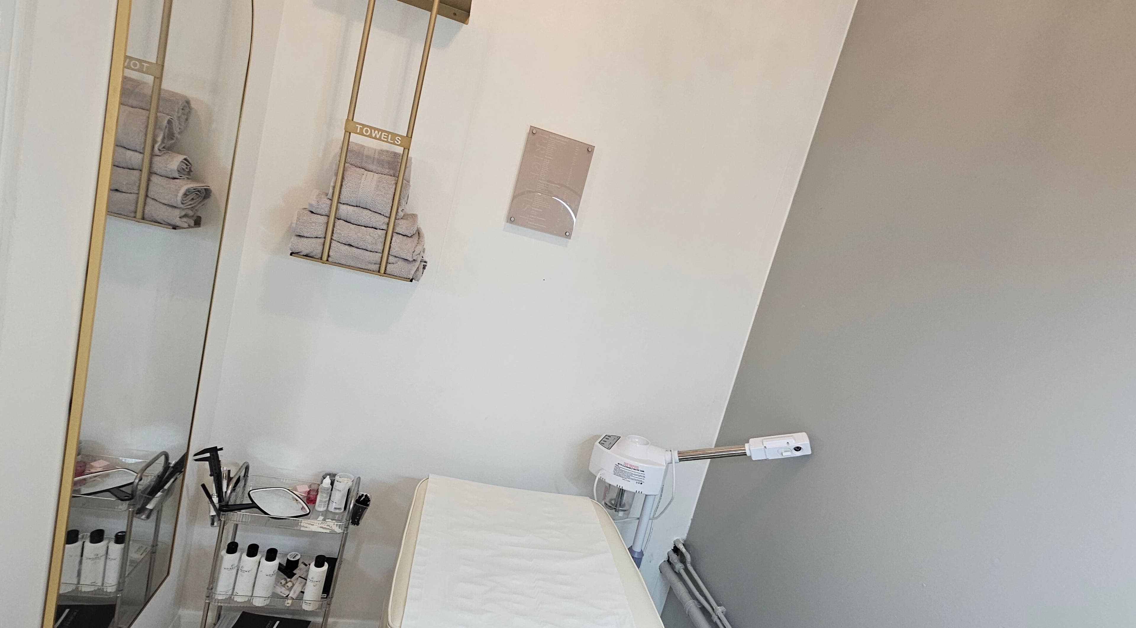 Treatment room at Pure Beauty Lounge in Hampton, England, GB with shelves, treatments, and towels.