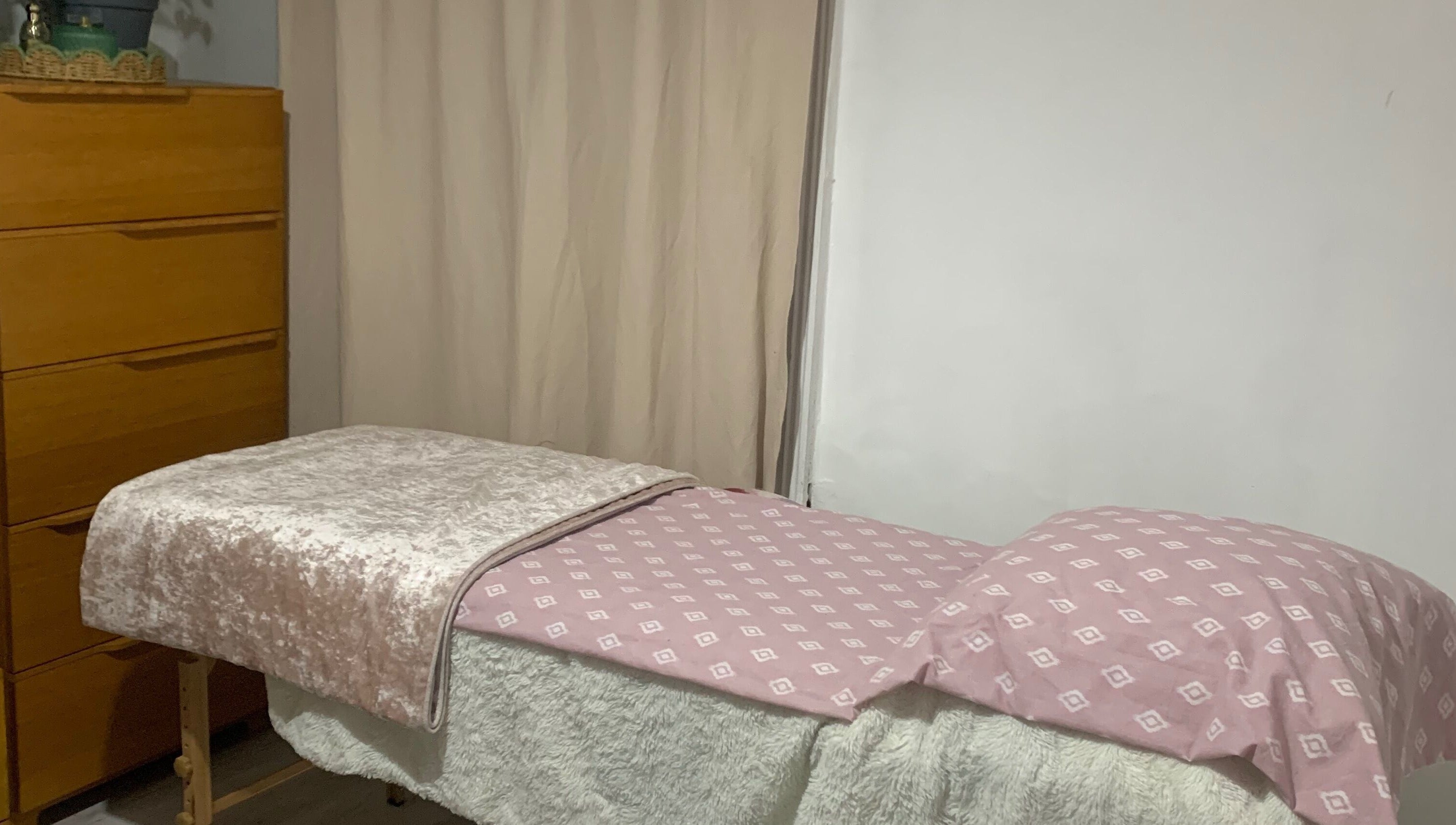 Cozy massage table at By Julia in Bedford, England, GB, featuring a soft pink patterned cover in a tranquil setting.