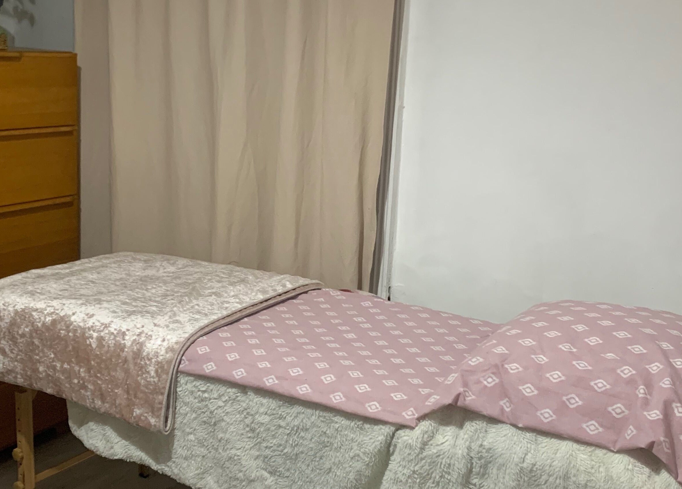 Cozy massage table at By Julia in Bedford, England, GB, featuring a soft pink patterned cover in a tranquil setting.