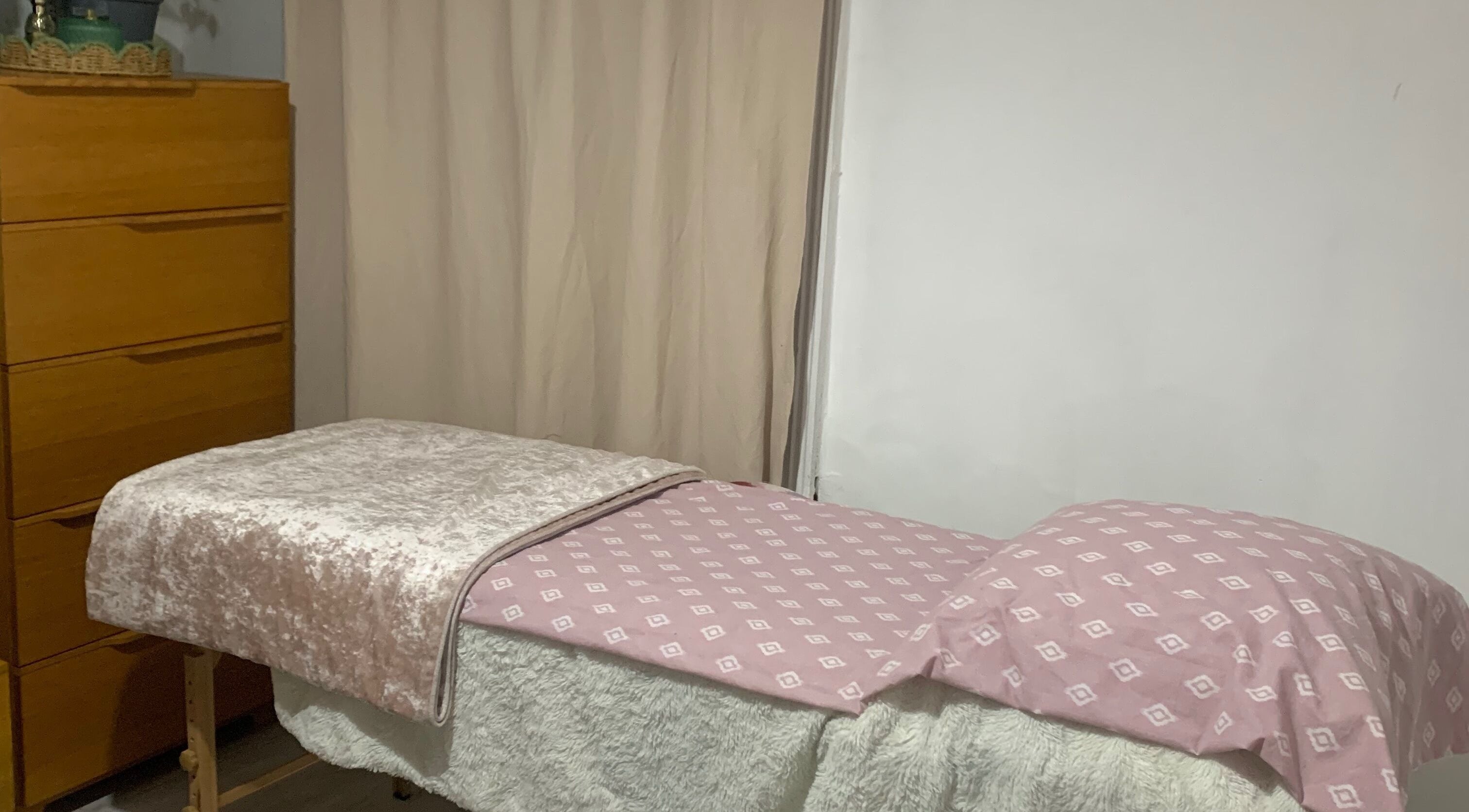 Cozy massage table at By Julia in Bedford, England, GB, featuring a soft pink patterned cover in a tranquil setting.