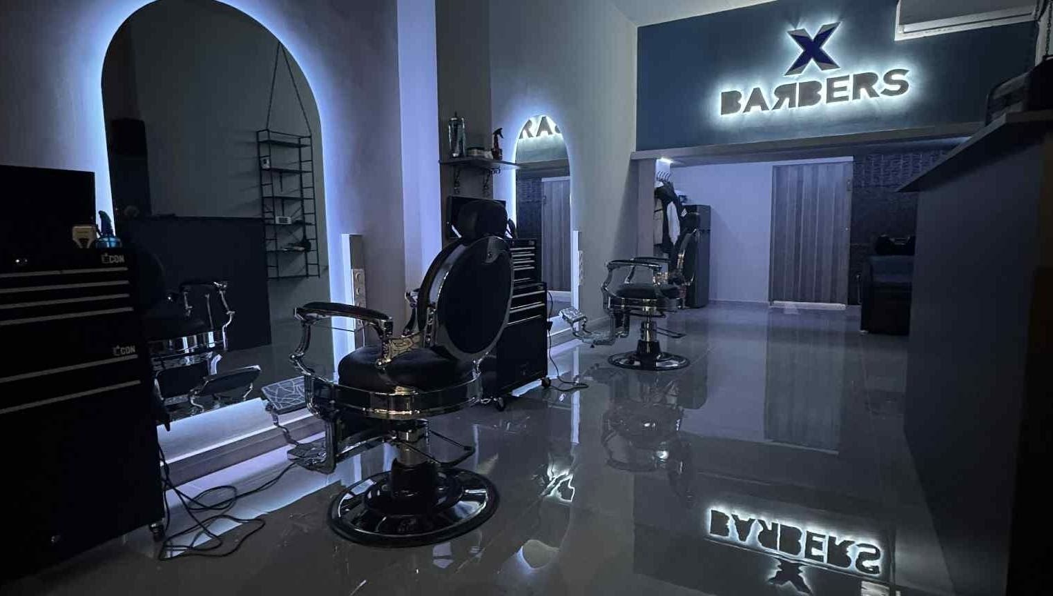 Εσωτερική άποψη της X BARBERS στη Λάρισα, GR με μοντέρνες καρέκλες και φωτισμό.