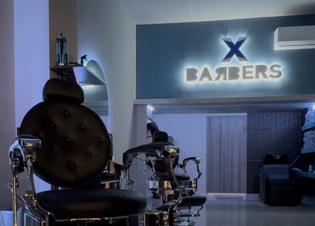 Σαλόνι X BARBERS στη Λάρισα, GR με φωτισμένη επιγραφή και πολυτελή καρέκλα κουρέματος.