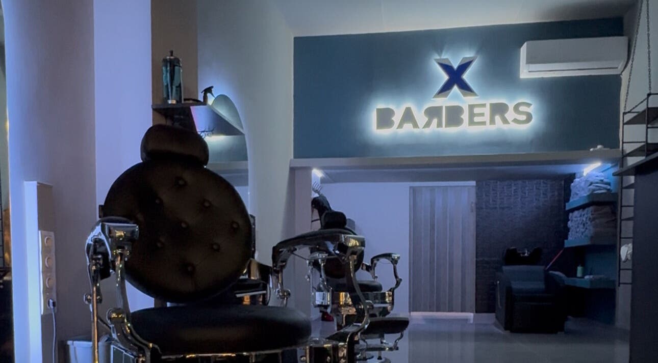 Σαλόνι X BARBERS στη Λάρισα, GR με φωτισμένη επιγραφή και πολυτελή καρέκλα κουρέματος.