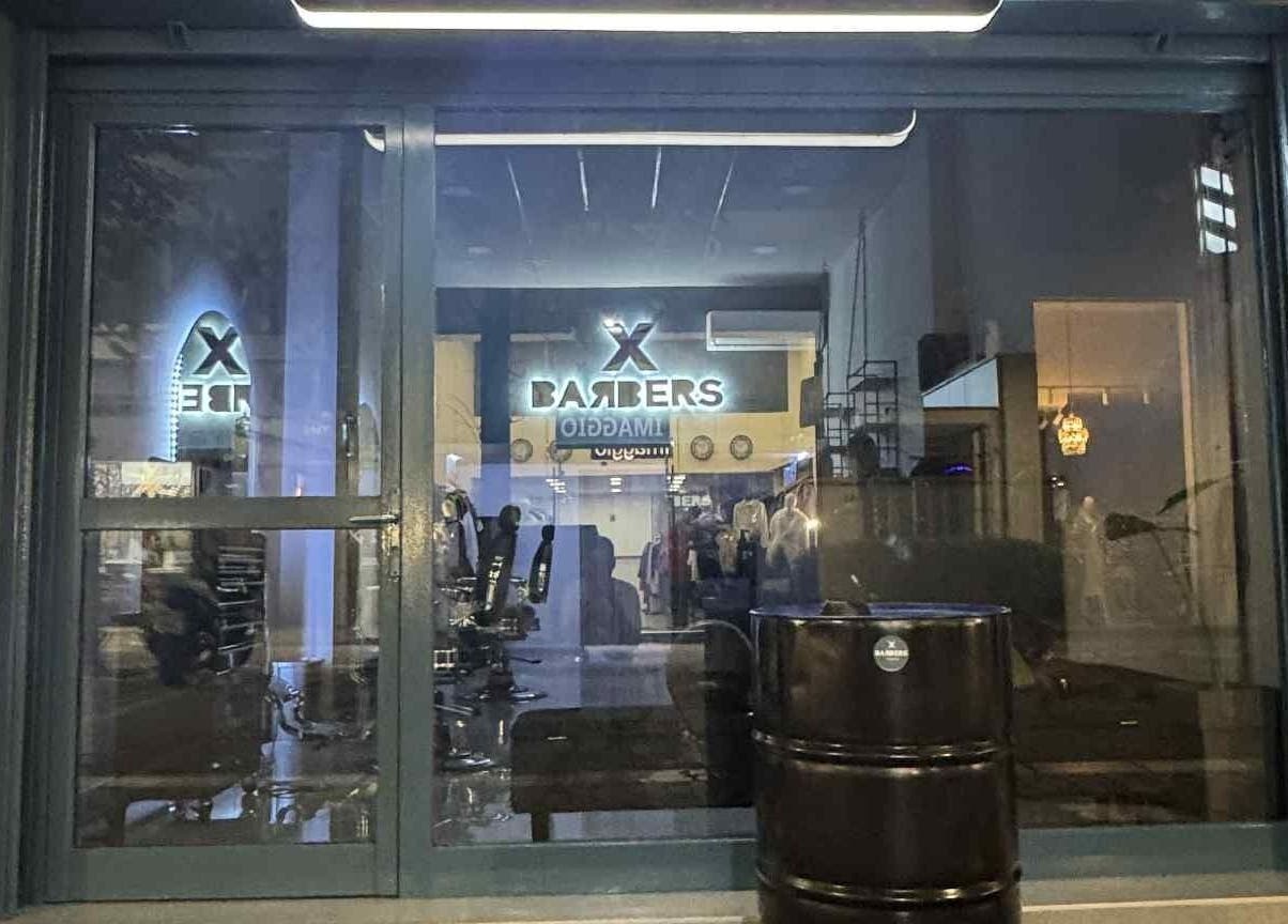 Φωτισμένη είσοδος του X BARBERS, Λάρισα, GR, με σύγχρονο εσωτερικό σχεδιασμό.