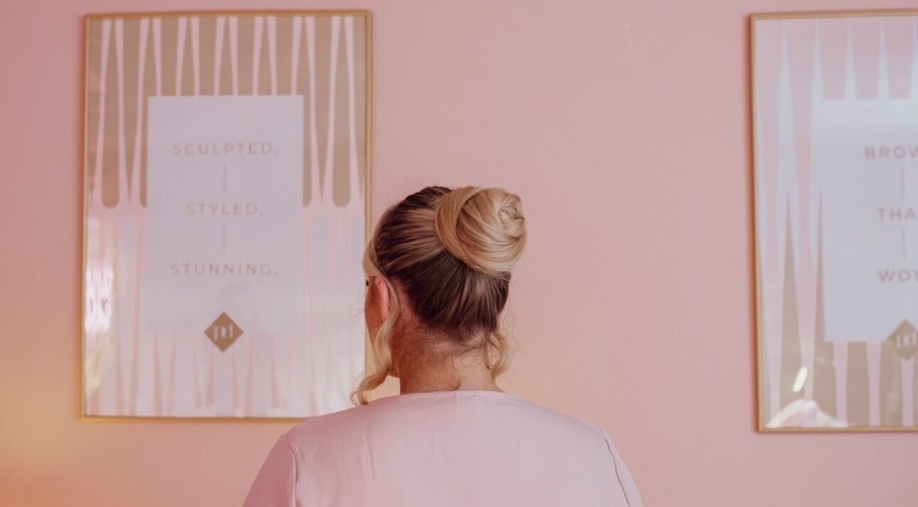 Woman with bun hairstyle at Plucked Beauty in Halifax, England, GB, surrounded by pink decor.