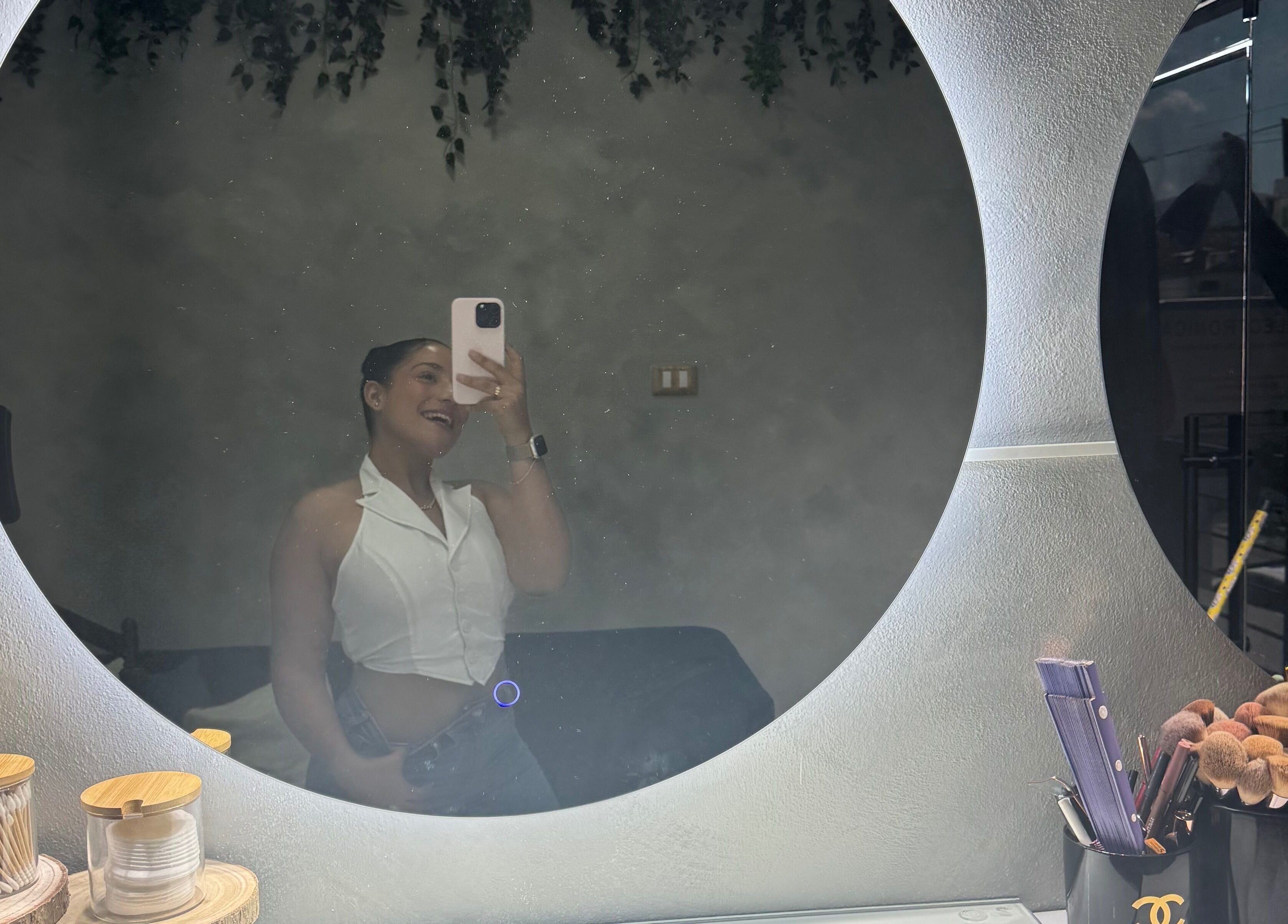 A woman smiling in a round mirror at By Nahil Study DEFINE TU BELLEZA, REALZA TU PODER in La Vega, La Vega, DO.