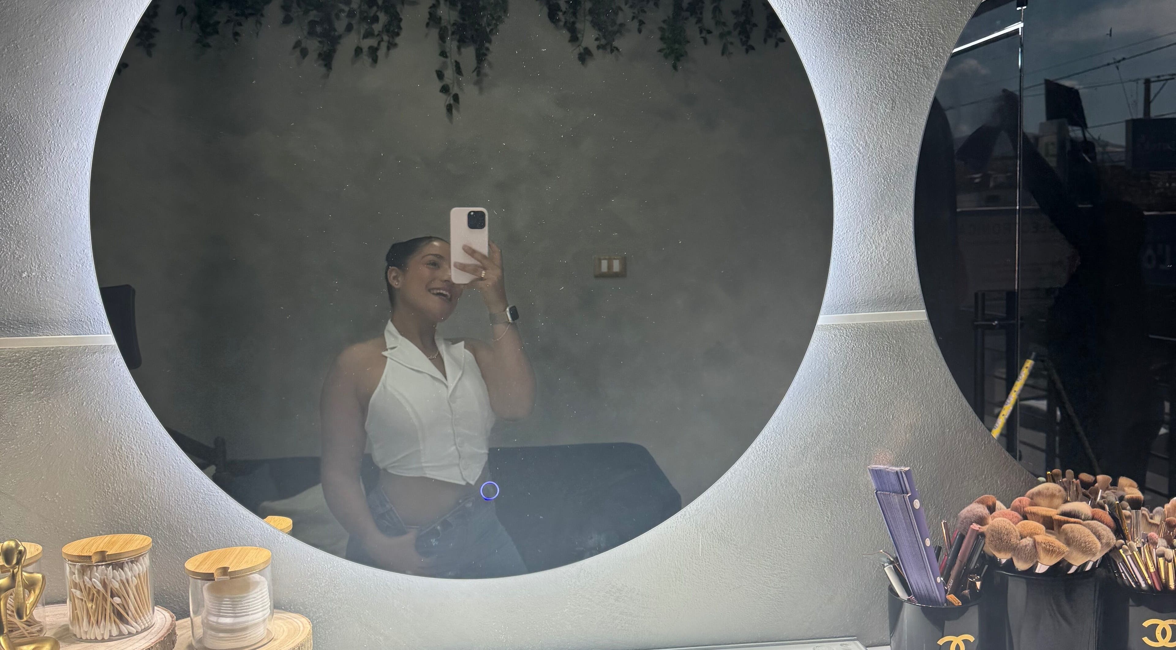 A woman smiling in a round mirror at By Nahil Study DEFINE TU BELLEZA, REALZA TU PODER in La Vega, La Vega, DO.