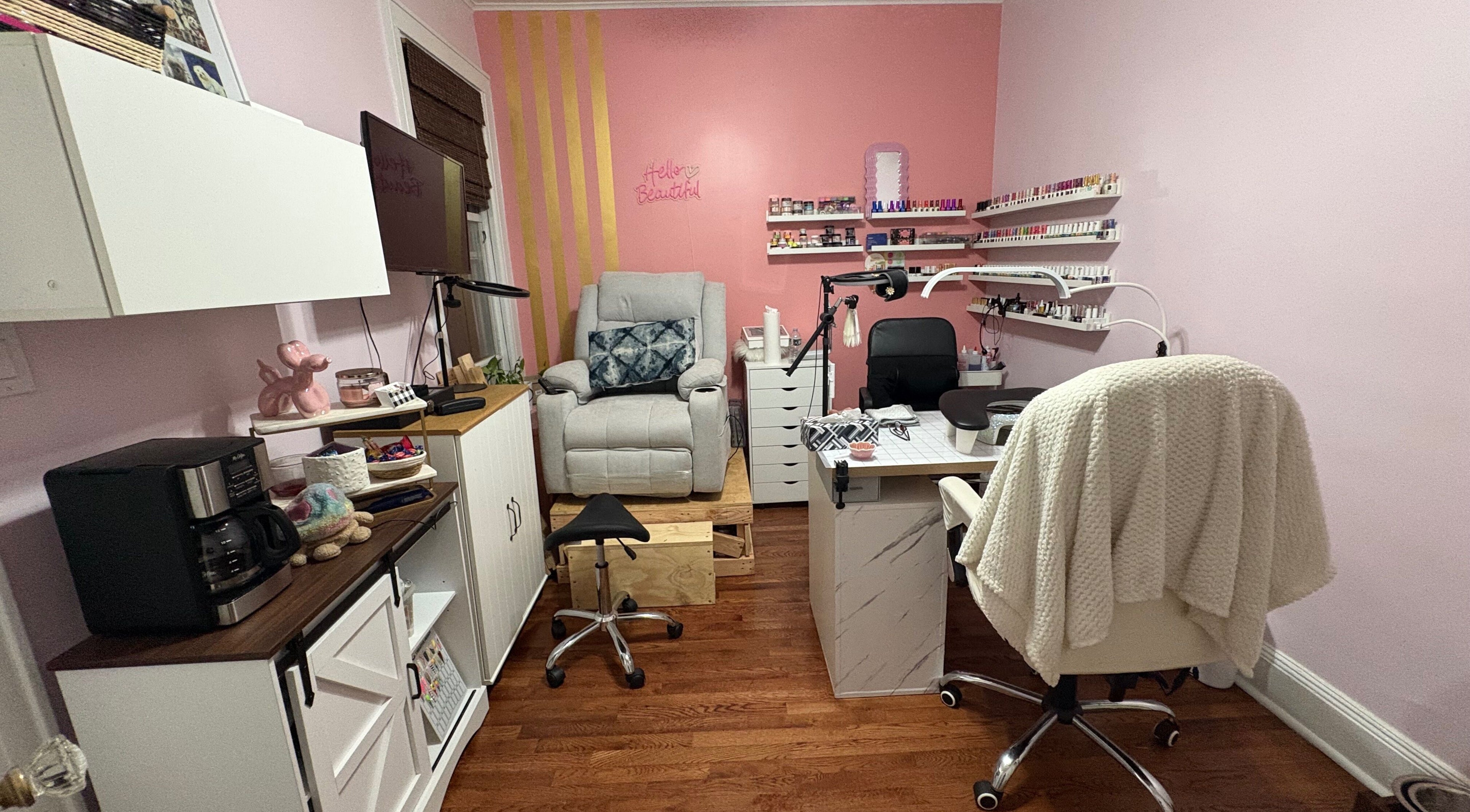 Cozy nail studio at Nailsbyflor in New York, featuring plush seating and a vibrant pink wall with polish displays.