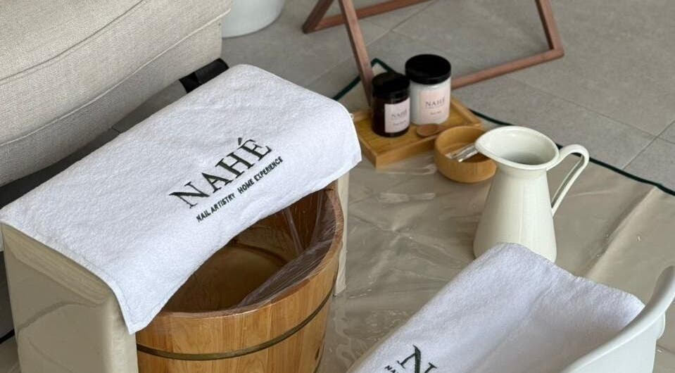 Foot spa setup at Nahé Beauty Home Service Salon, Dubai, AE, featuring towels and a wooden bucket.