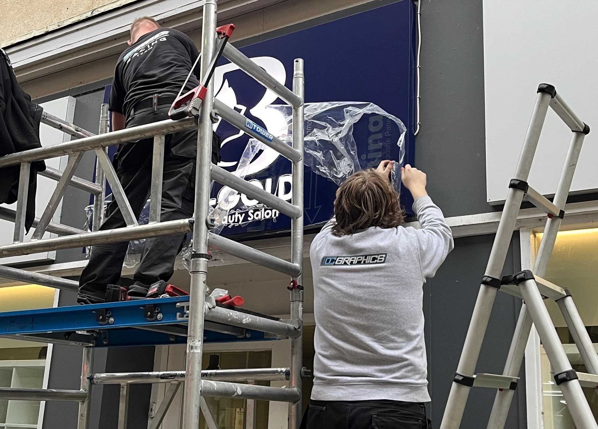 Workers installing Bim-Gold hair and beauty salon sign in Huddersfield, England, GB.
