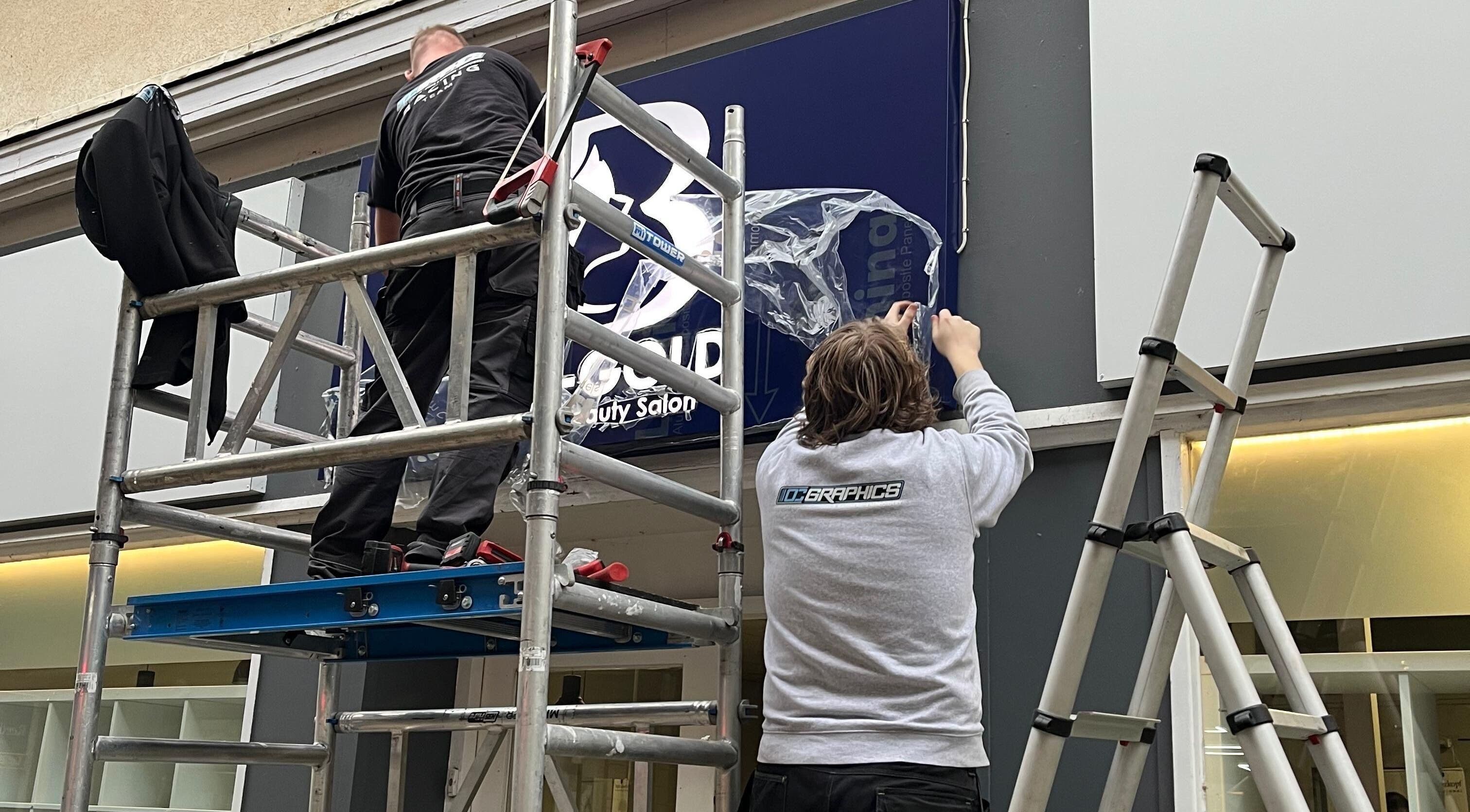 Workers installing Bim-Gold hair and beauty salon sign in Huddersfield, England, GB.