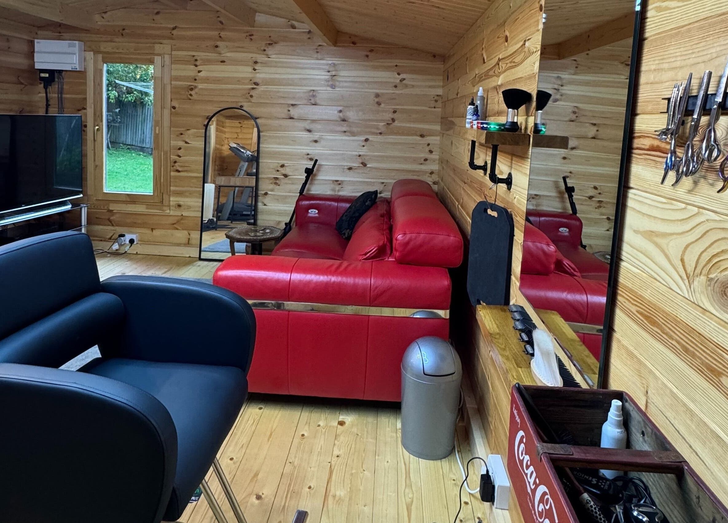 Inviting barber space at Barbering by Teegs in Hawkhurst, England, GB with modern chair and red sofa.