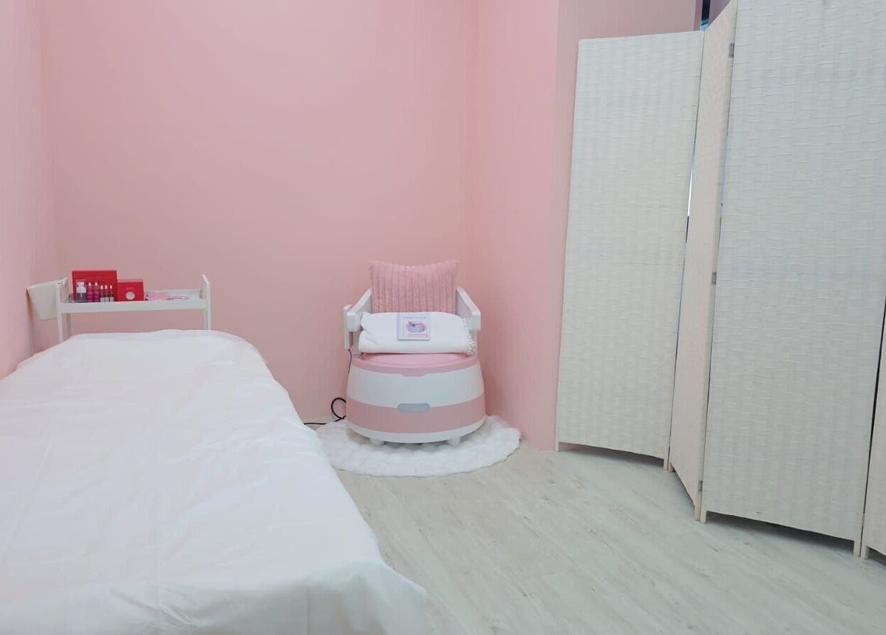 Blossom Glow's serene pink treatment room in Singapore, SG, showcasing a relaxing chair and cozy bed.