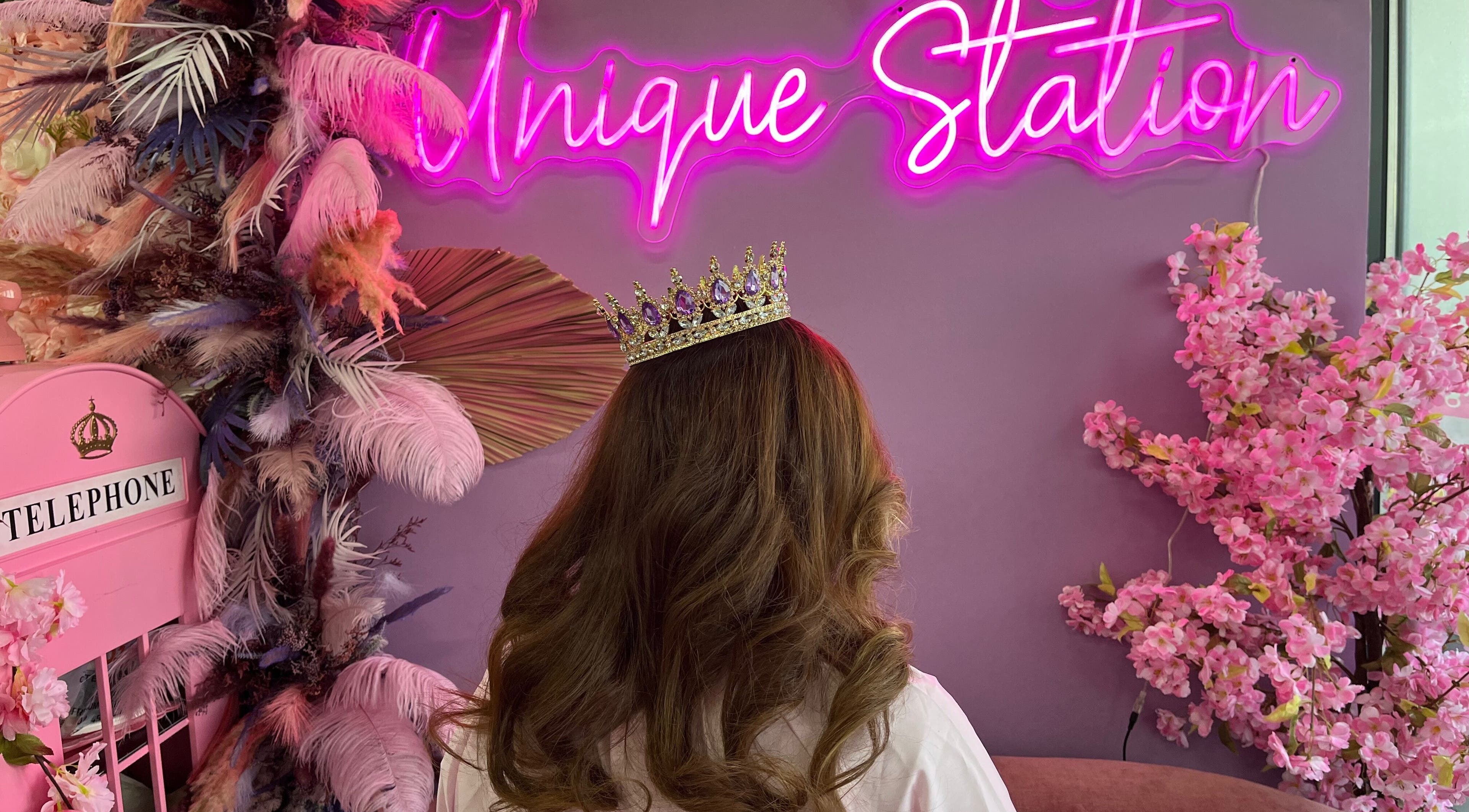 Back view of woman with crown at Unique Station Beauty Salon, Dubai, AE. Vibrant floral decor and pink neon sign.