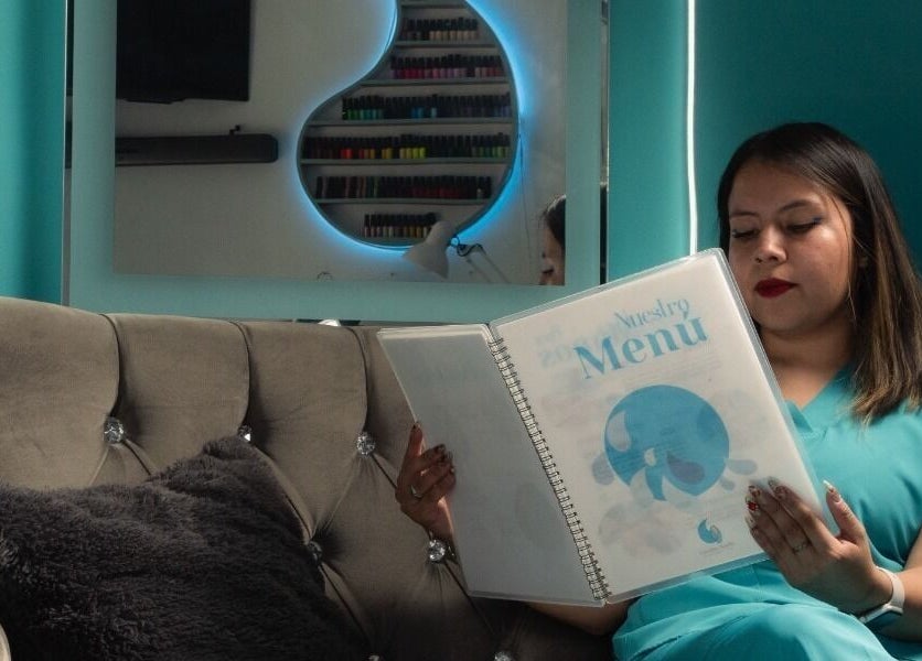 Cliente en Gotita Nails, Ciudad De México, revisando menú de servicios en elegante sala de espera.