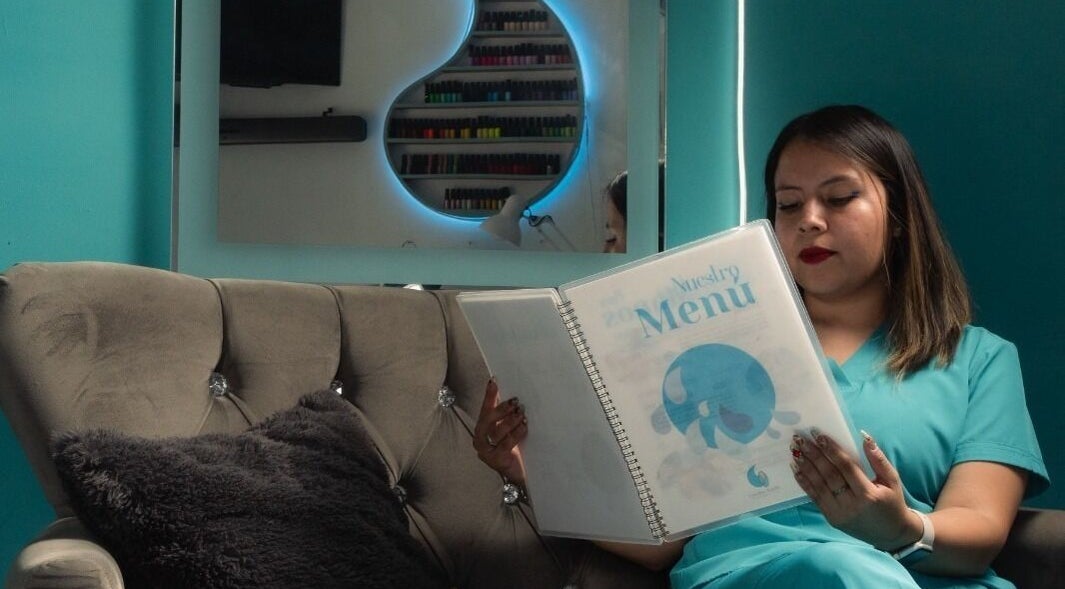 Cliente en Gotita Nails, Ciudad De México, revisando menú de servicios en elegante sala de espera.