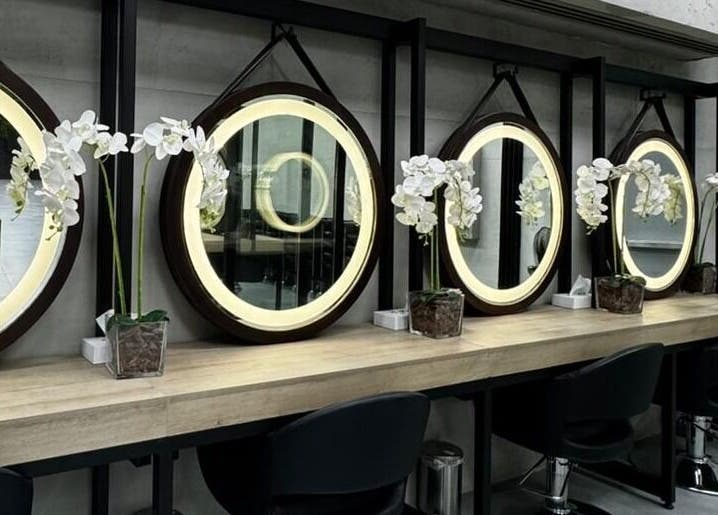 تصميم داخلي عصري في Brazil Studio Salon - Riyadh، الرياض، مقاطعة الرياض، SA يعرض مرايا دائرية وأزهار بيضاء.