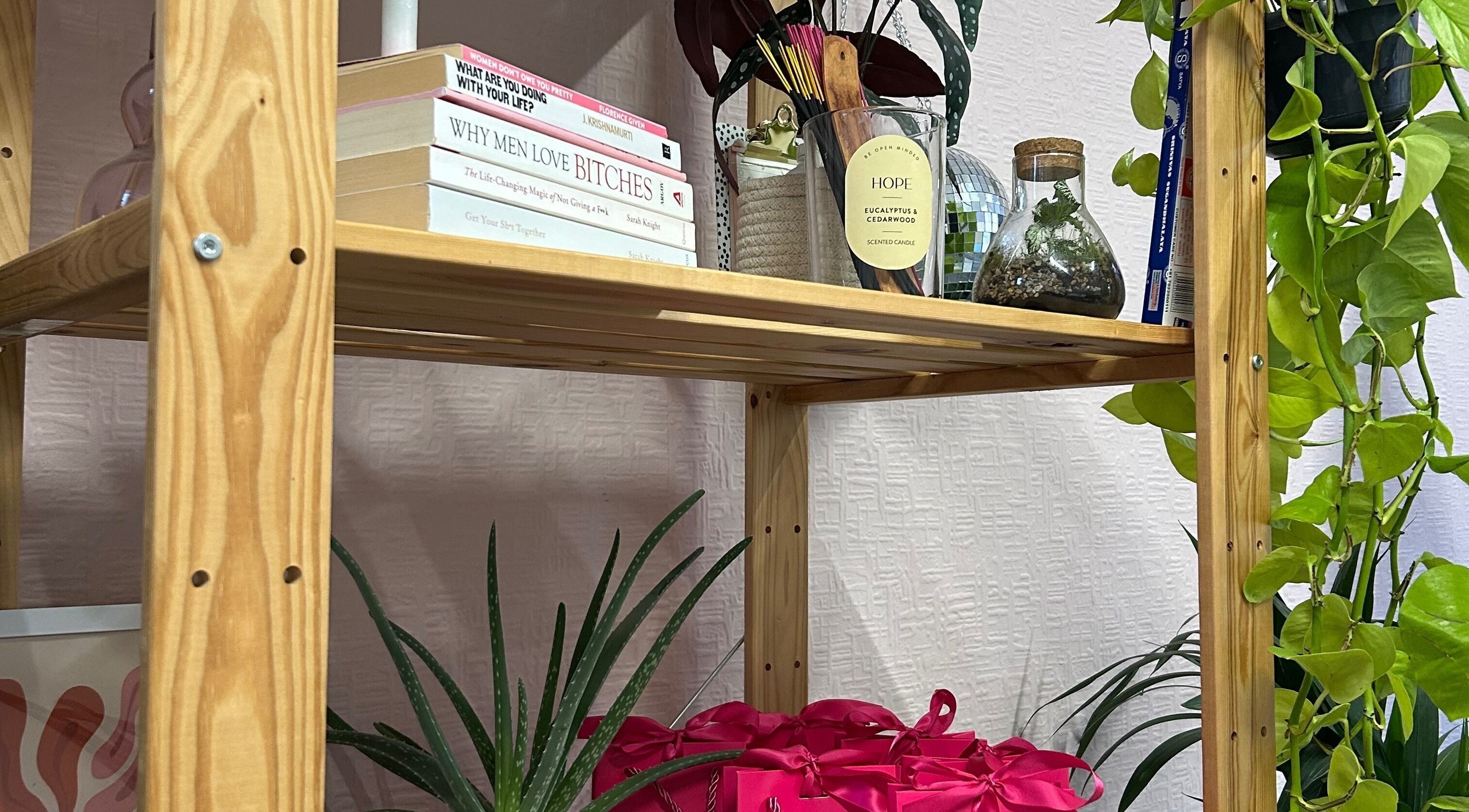 Wooden shelf at By Ianthe in Melton Mowbray, England, GB, adorned with books, plants, and a candle.