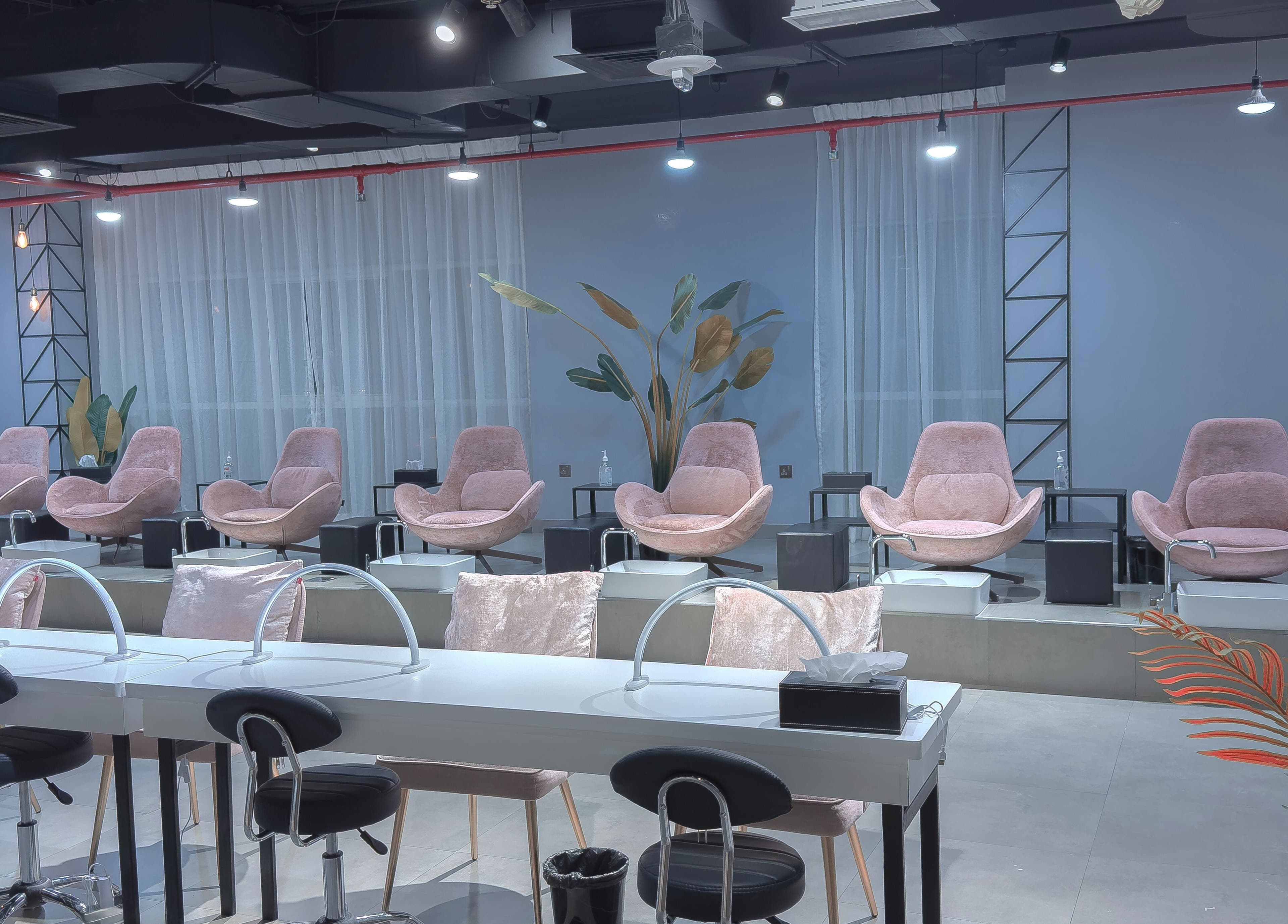 Modern interior of Painted Nails Beauty Salon in Abu Dhabi, AE with plush pink chairs and sleek manicure stations.