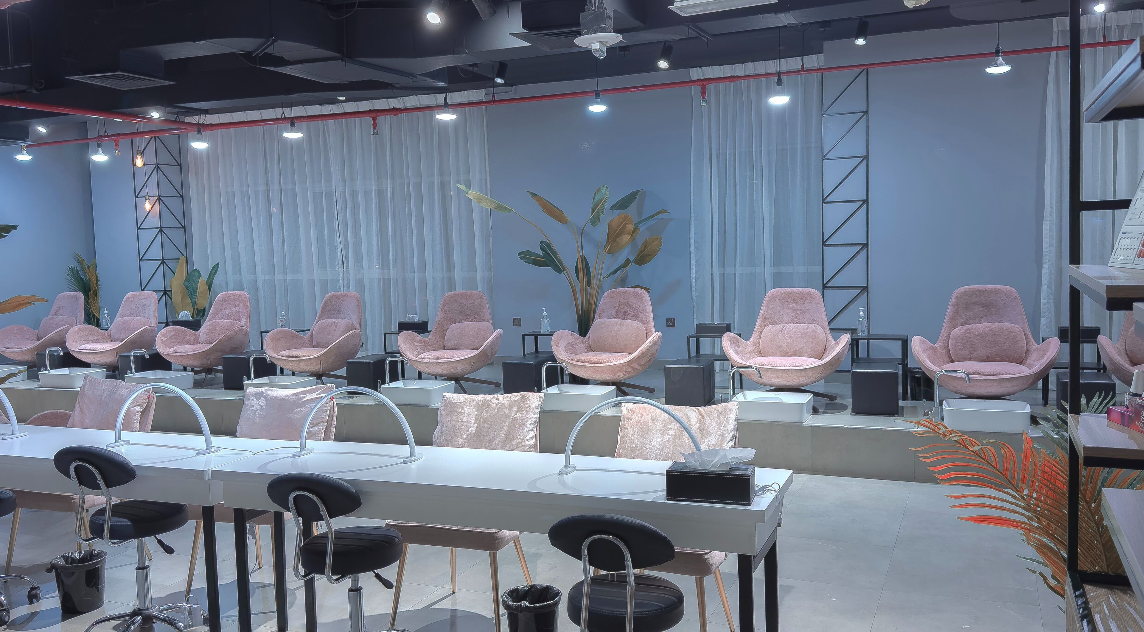 Modern interior of Painted Nails Beauty Salon in Abu Dhabi, AE with plush pink chairs and sleek manicure stations.