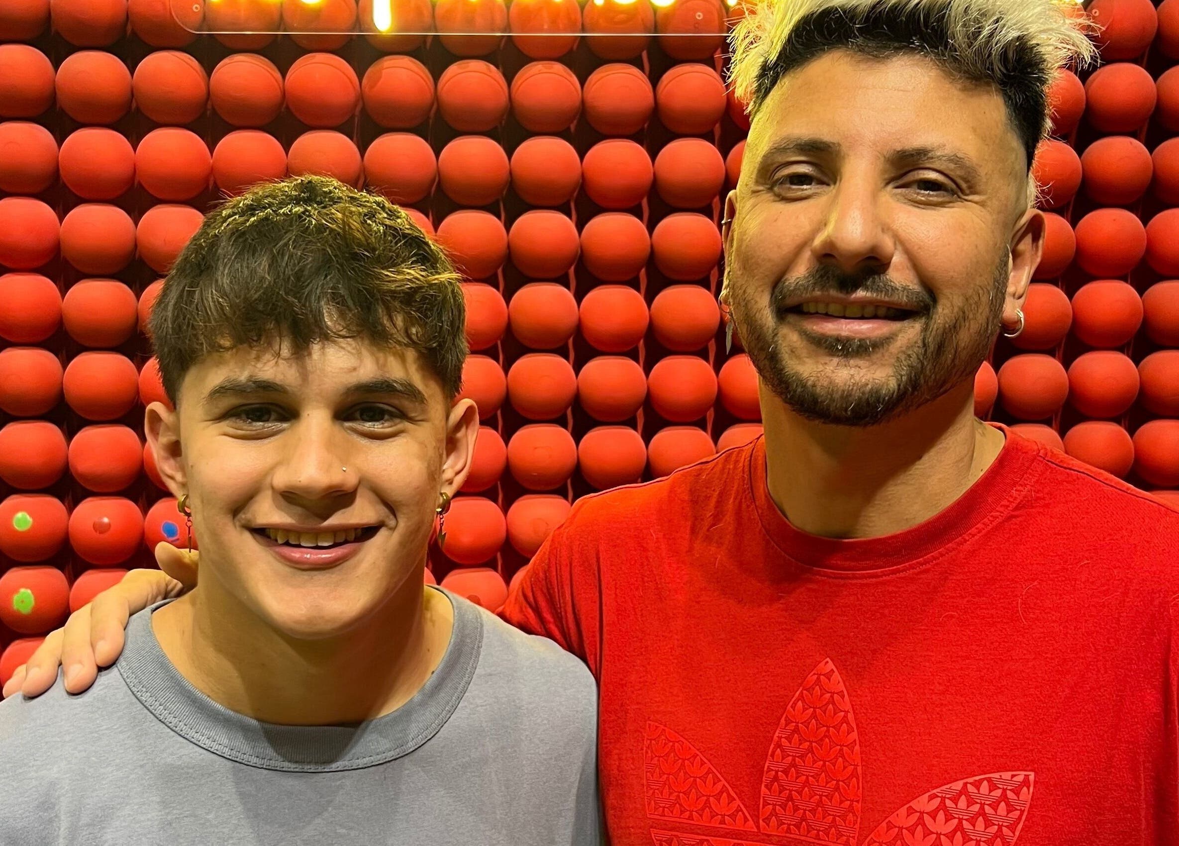 Two smiling individuals at Chispa Barberia, Córdoba, AR, with a unique red ball wall backdrop.