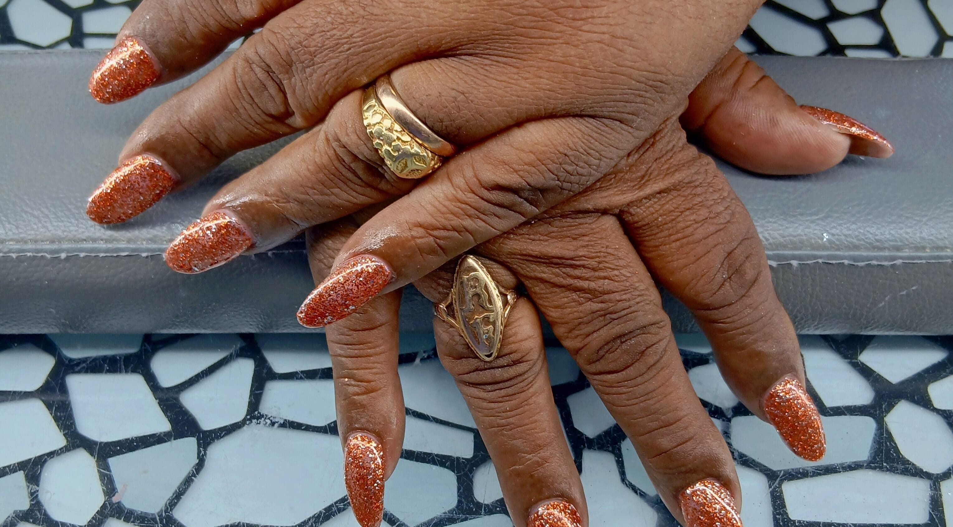 Glittering orange nails with gold rings at Golden Phoenix Nails in Koolbaai, Sint Maarten, SX.