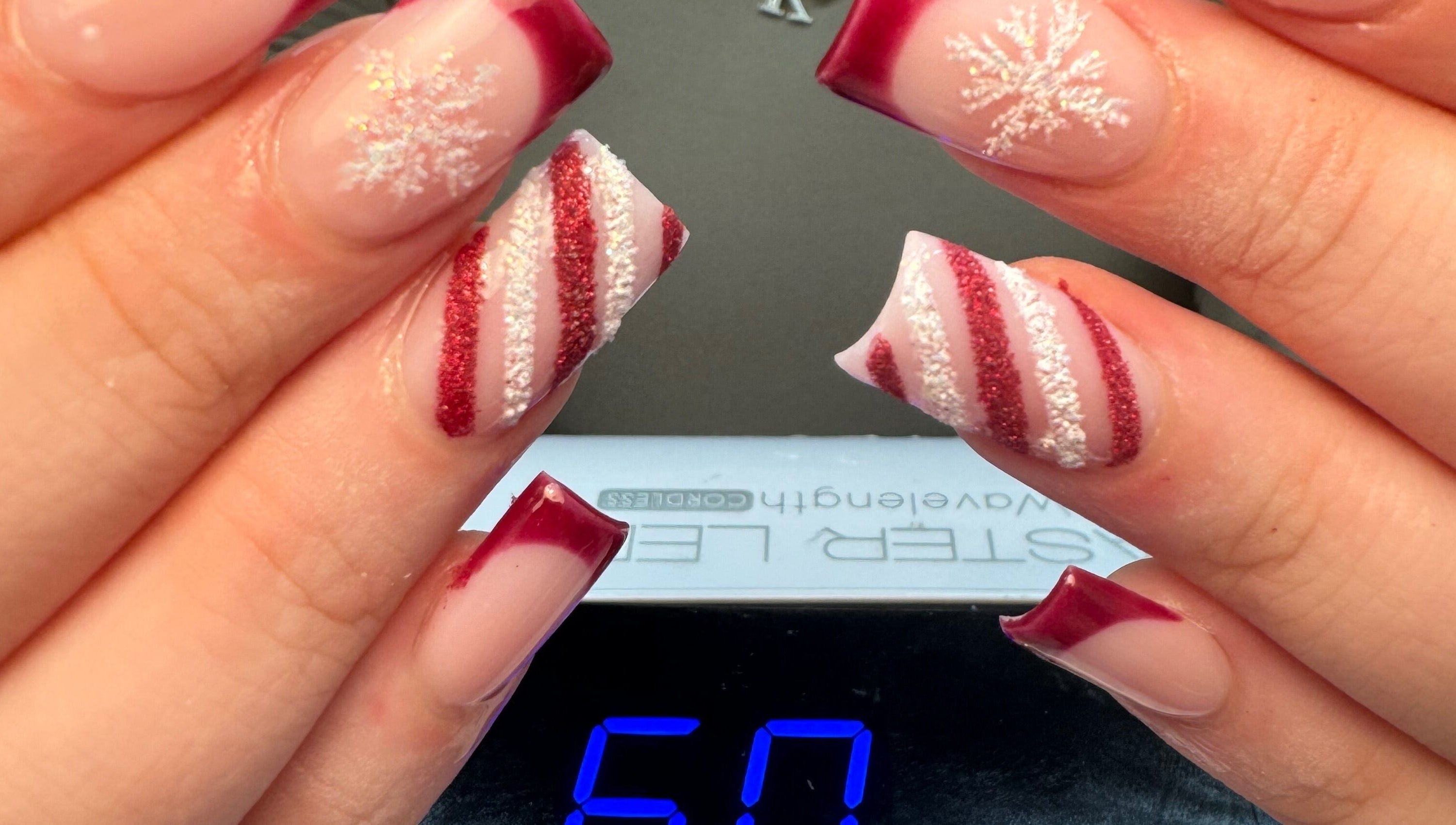 Mẫu móng tay nghệ thuật với họa tiết tuyết và sọc đỏ tại Natural Nail, Birmingham, England, GB.