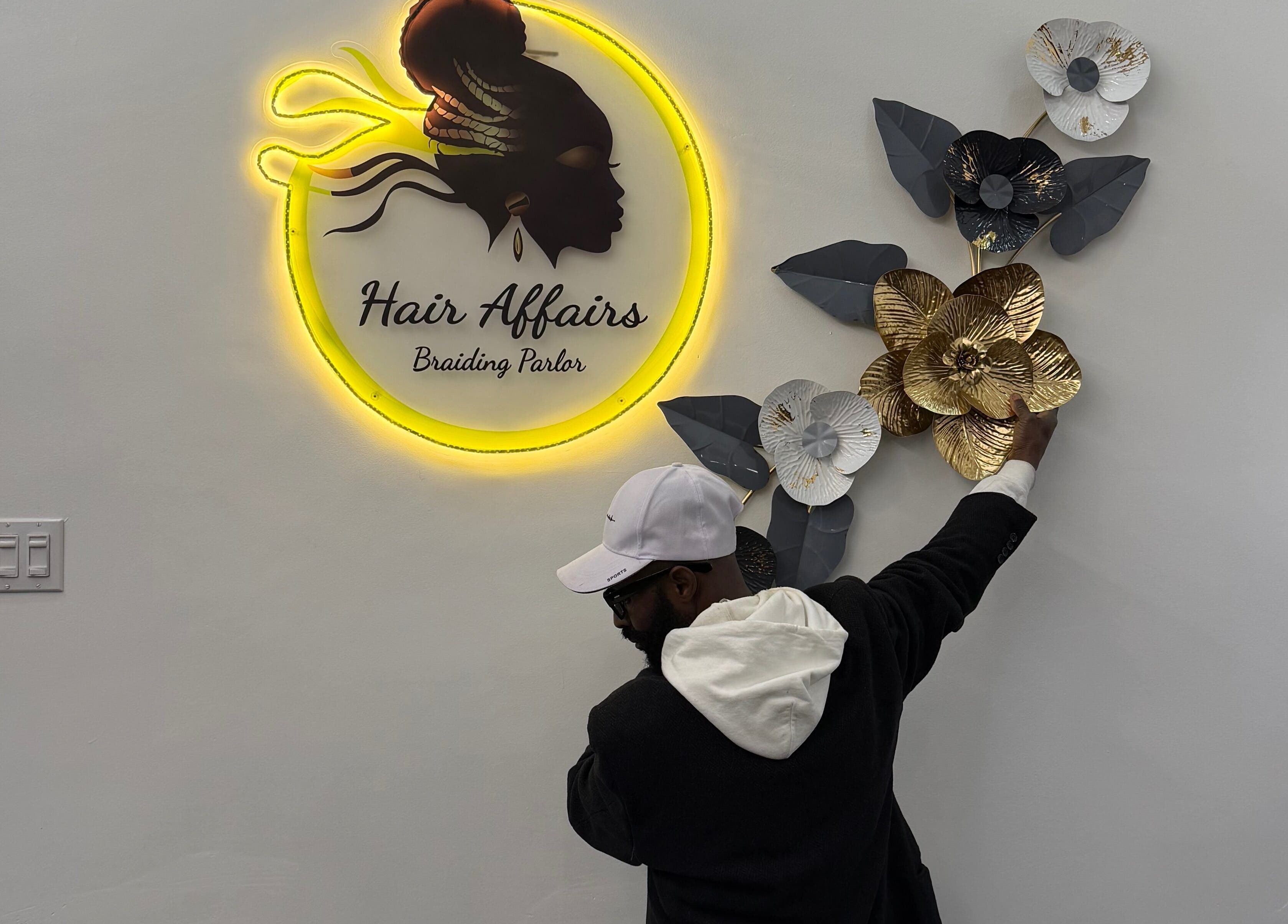 Man decorating wall at Hair Affairs Braiding Parlor, Toronto, Ontario, CA with illuminated logo and floral art.
